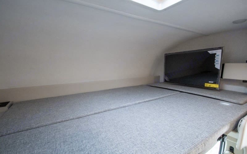 This RV rental interior shows a light-colored sleeping berth with grey cushions and a flat-screen TV on the right for entertainment.. Thor four winds 2026