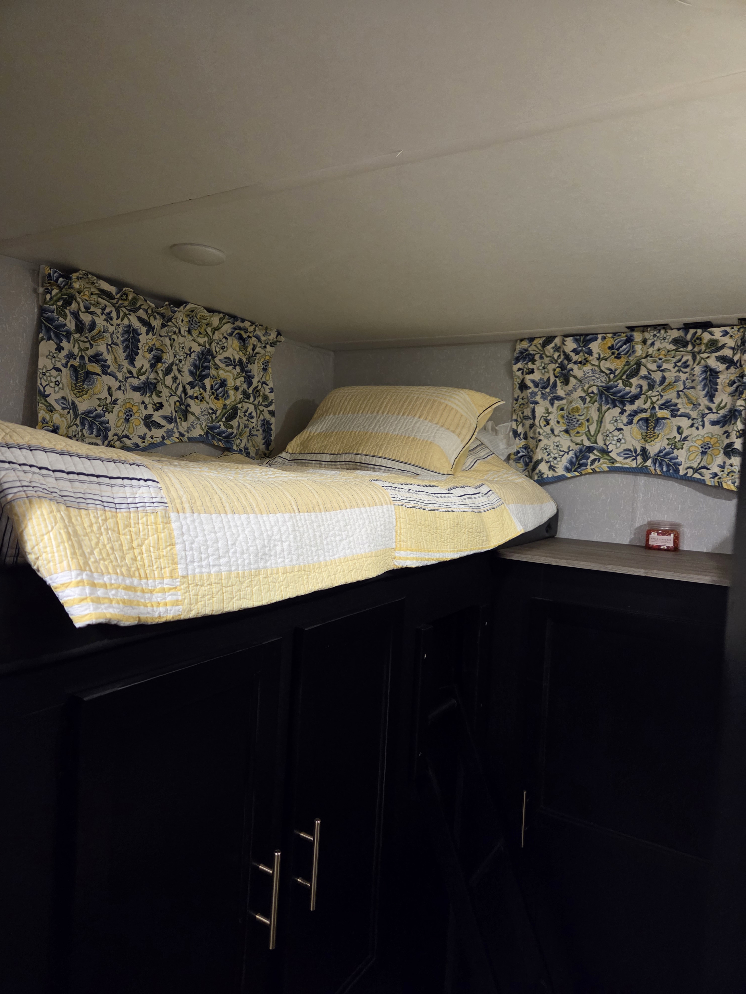 Cozy RV rental bunk bed with a yellow quilt, floral curtains, and dark cabinets, offering comfortable sleeping.. Forest River Cherokee Grey Wolf Special Edition 2021