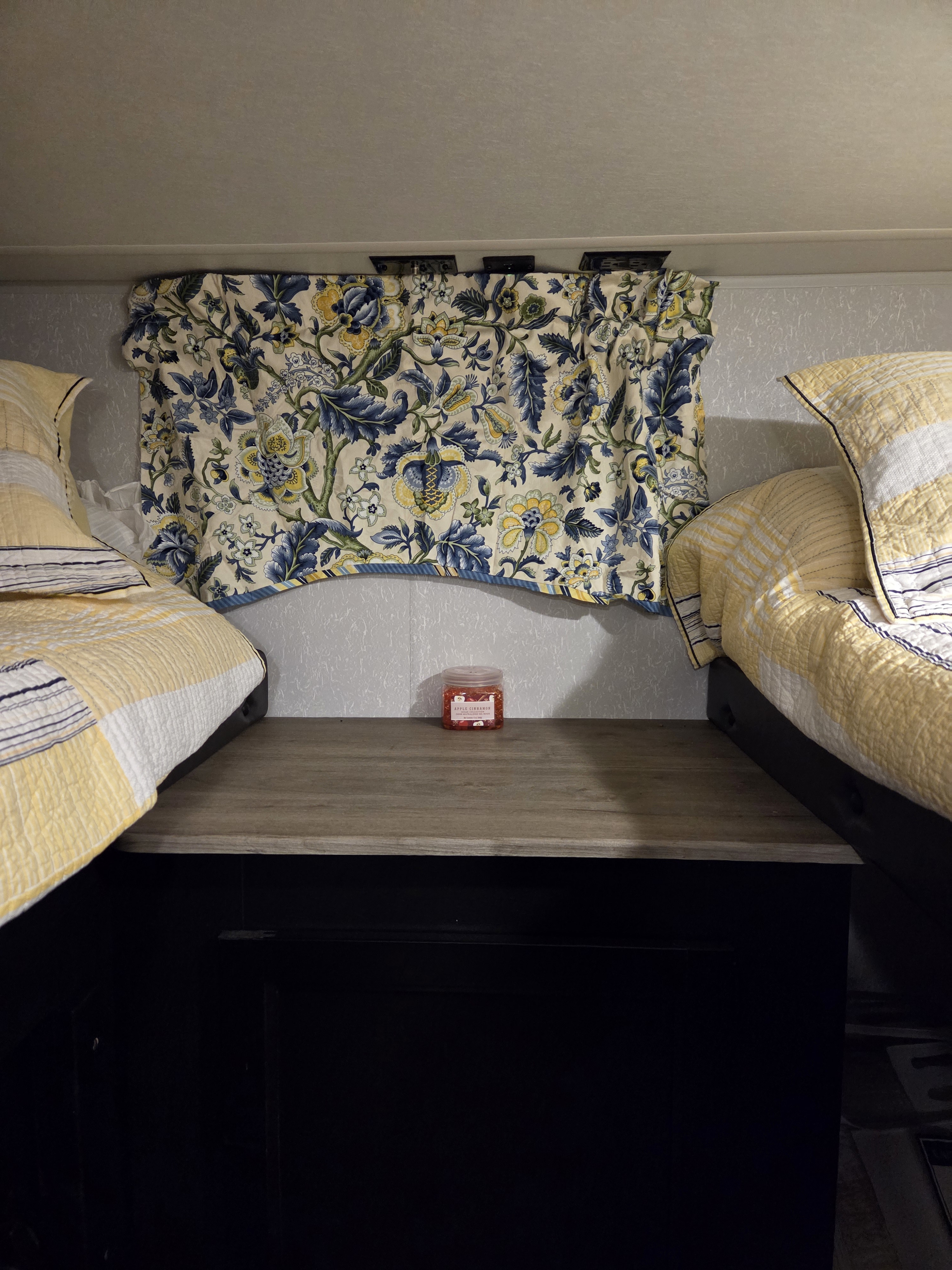 RV rental bunk beds with cozy yellow bedding, floral curtains, and a shelf holding apple cinnamon potpourri, offering compact comfort.. Forest River Cherokee Grey Wolf Special Edition 2021