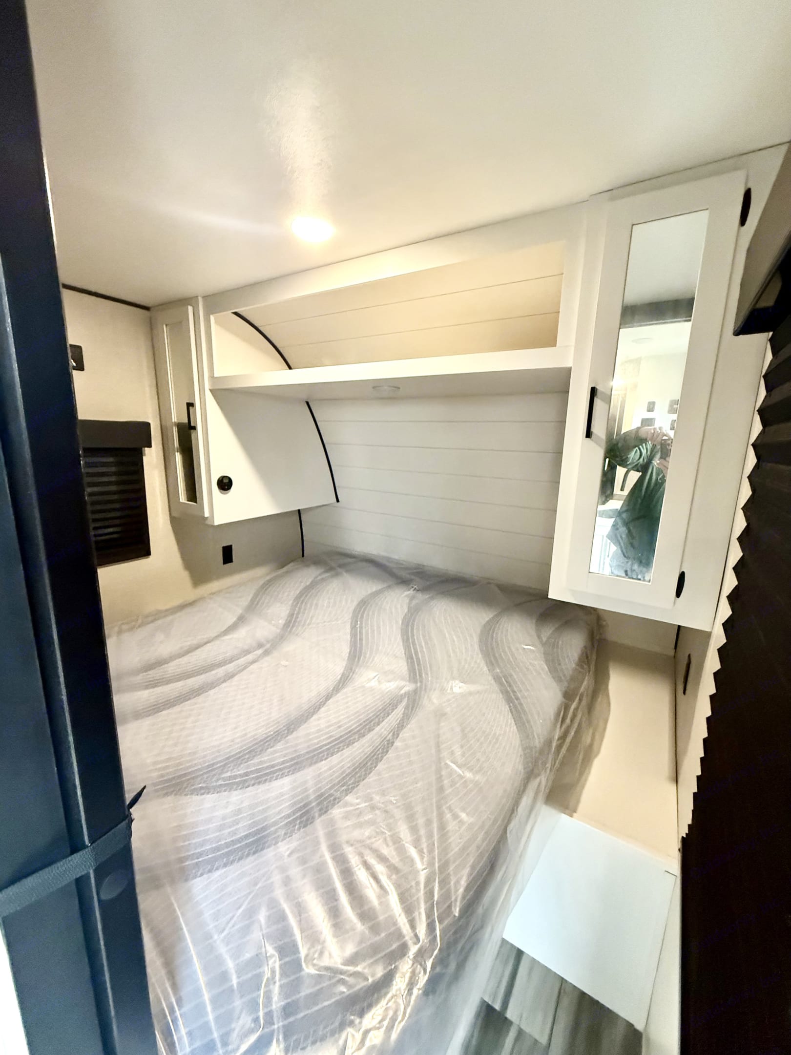 This cozy rv rental bedroom features a new, plastic-covered mattress, built-in storage, and modern white interior.. Highland Ridge RV Open Range 2024