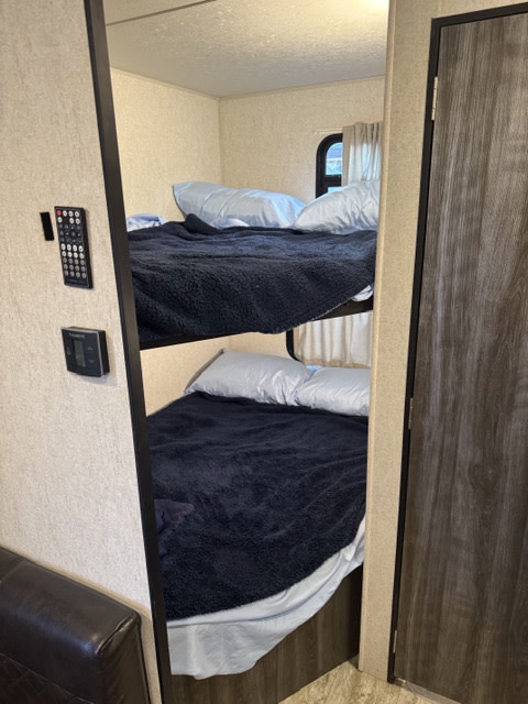 Cozy bunk beds ready in this RV rental, featuring soft bedding, a window, and wall controls for comfortable travel.. Highland Ridge RV Open Range 2019