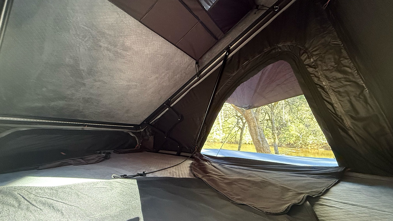 This RV rental's rooftop tent offers a sleeping area, integrated lighting, and a beautiful window view of trees & water.. Cedar Ridge Deneb XT 2025