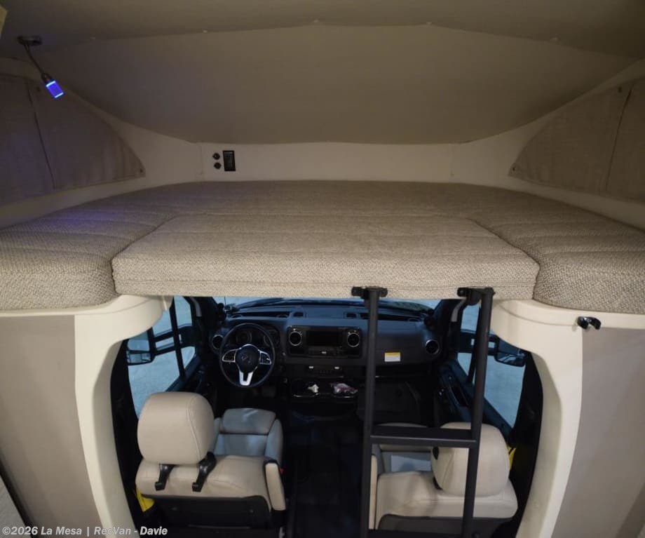 RV rental interior view shows a comfortable cab-over bunk bed, with an access ladder descending to the vehicle's cockpit and front seats.. Winnebago View 2021