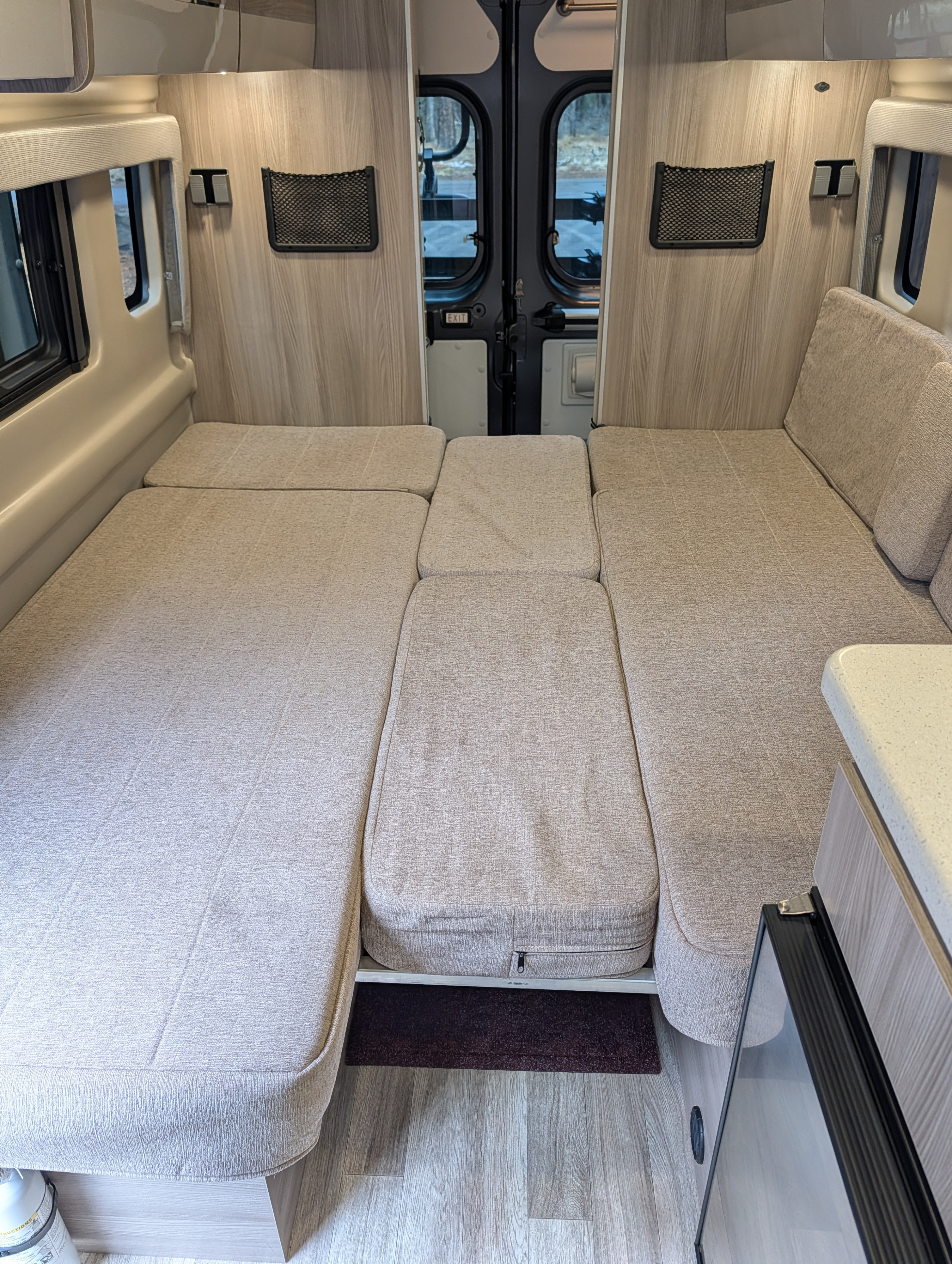 Versatile camper van interior, set up as a bed/lounge, ideal for an rv rental. Cushioned seating and rear doors visible.. Thor Tellaro 2024