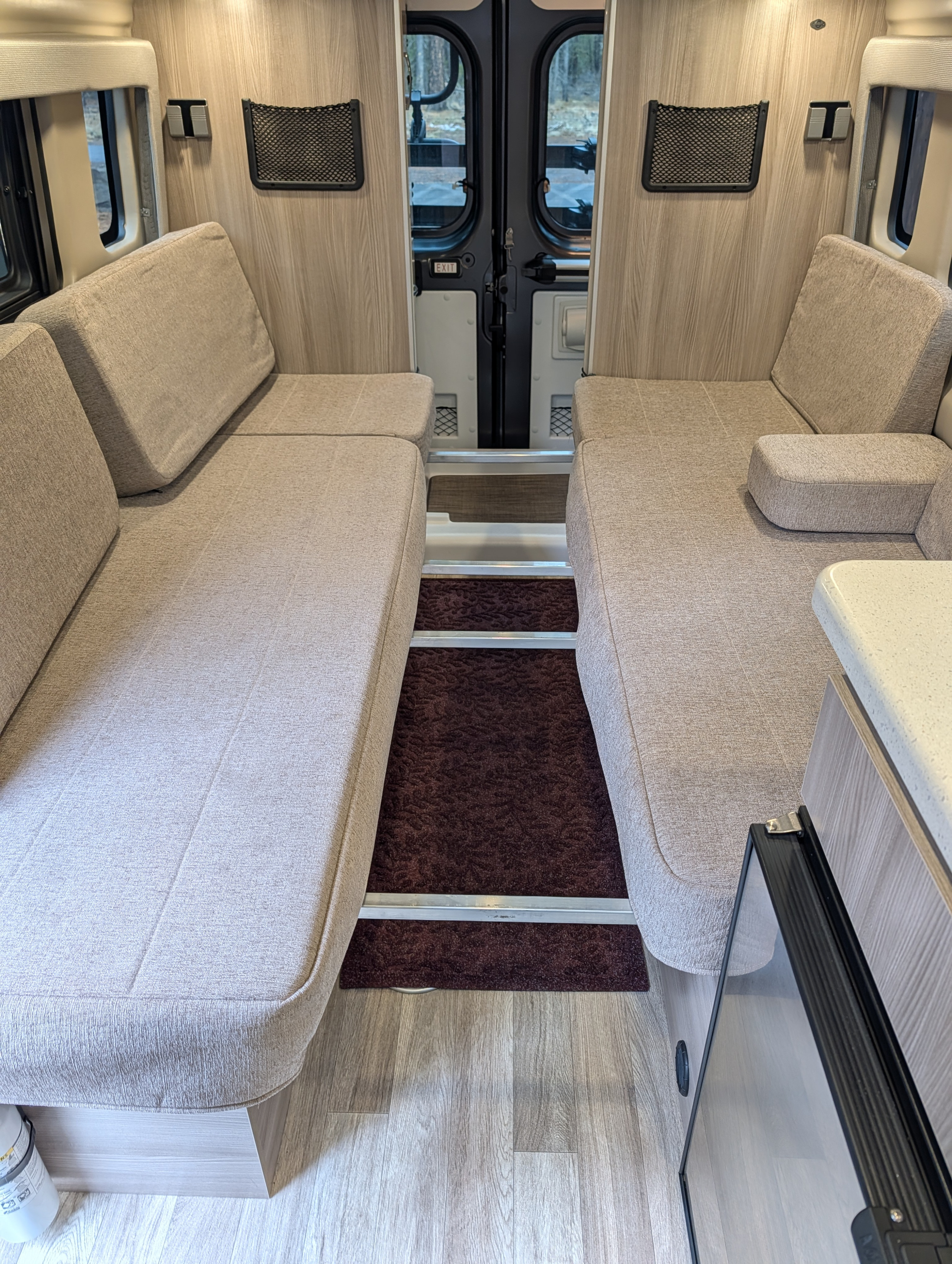 RV rental interior features two light beige cushioned benches that convert to beds, a central aisle with steps, and rear exit doors.. Thor Tellaro 2024