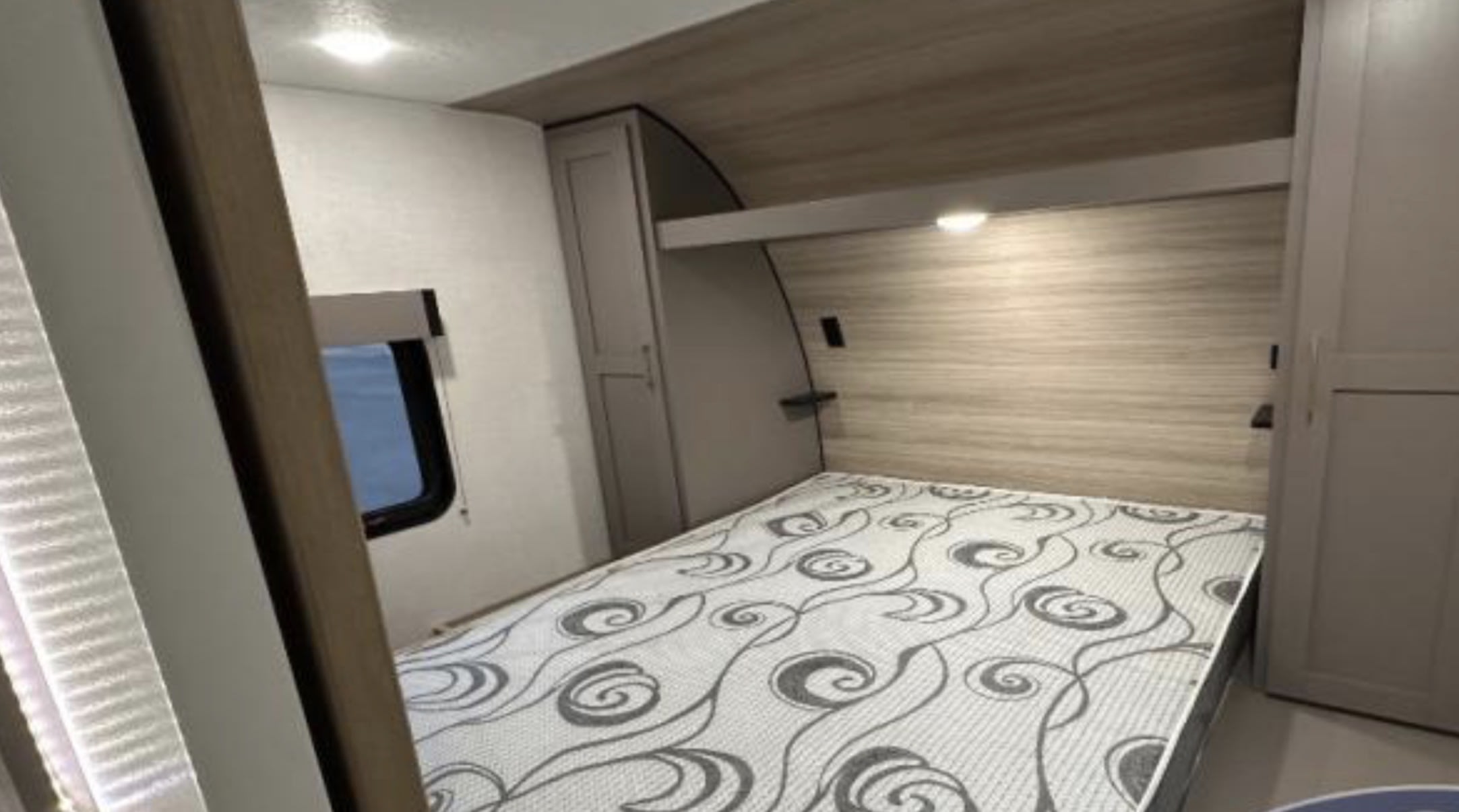 Compact RV rental bedroom with a patterned mattress, overhead storage, and cabinet space for a cozy travel experience.. KZ Sportsmen SE 2025