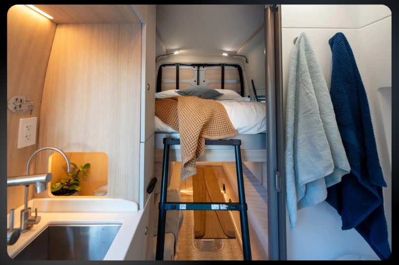 Modern rv rental interior: compact kitchen, elevated bunk bed with ladder, and towels. Ideal for road trips.. Noovo Plus 2026