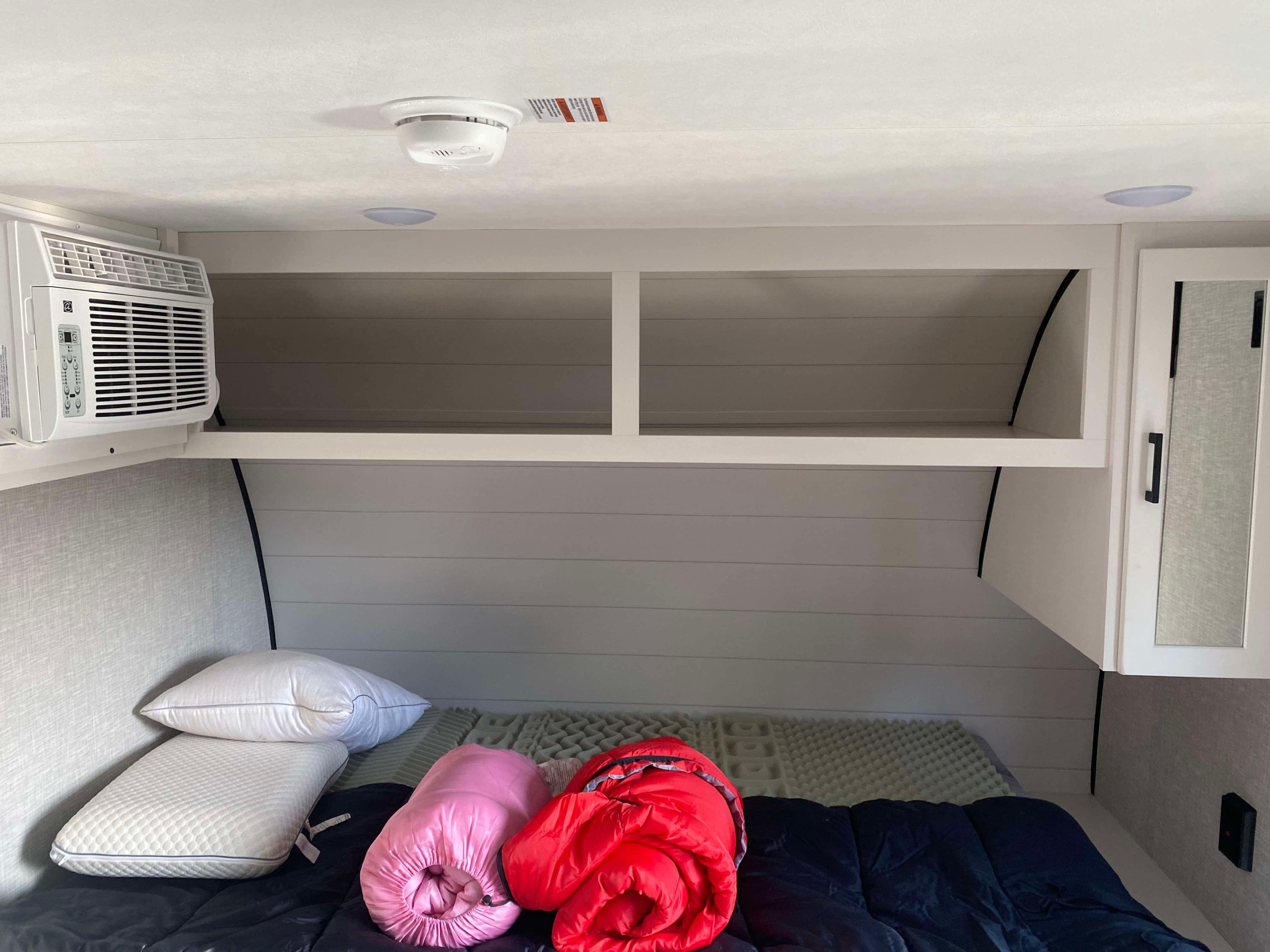 RV rental bedroom interior: bed, pillows, sleeping bags, wall AC, overhead shelves, and a ceiling smoke detector.. Jayco Jay Flight SLX STX Edition 2025