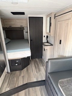 View inside an RV rental: light wood-toned interior with a bed, vanity sink, and dinette seating area.. Forest River Sunseeker LE 2024