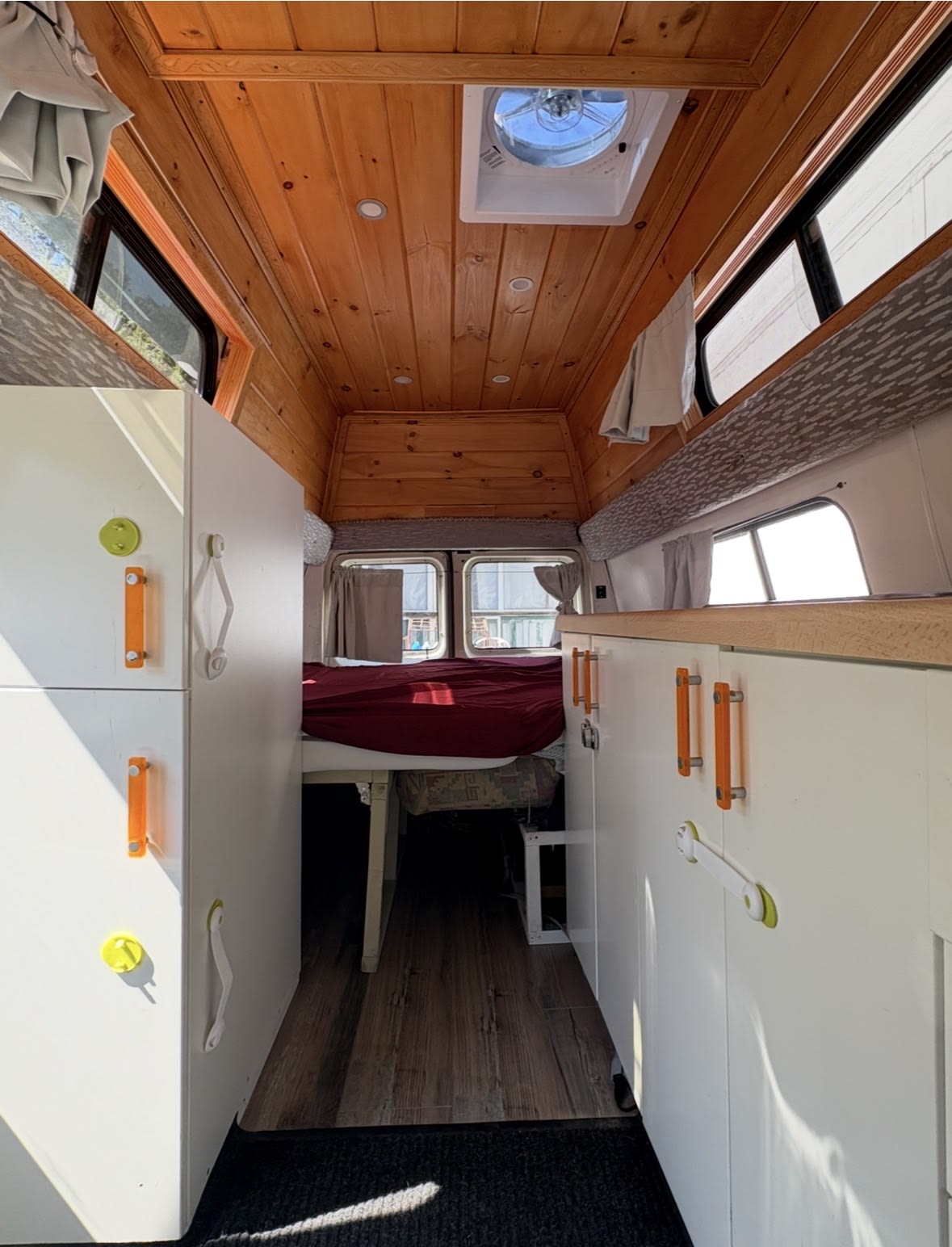 Bright RV rental interior: wooden ceiling, white cabinets with colorful handles, and a red-covered bed await your adventures.. Ford Econoline Club Wagon 1994