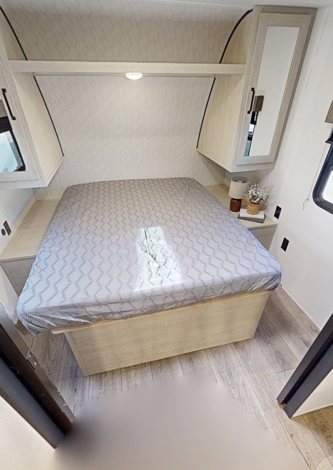 Cozy RV rental bedroom featuring a full bed with patterned sheets, overhead storage, and bedside tables on light wood floors.. Forest River Palomino Puma Camping Edition 2025