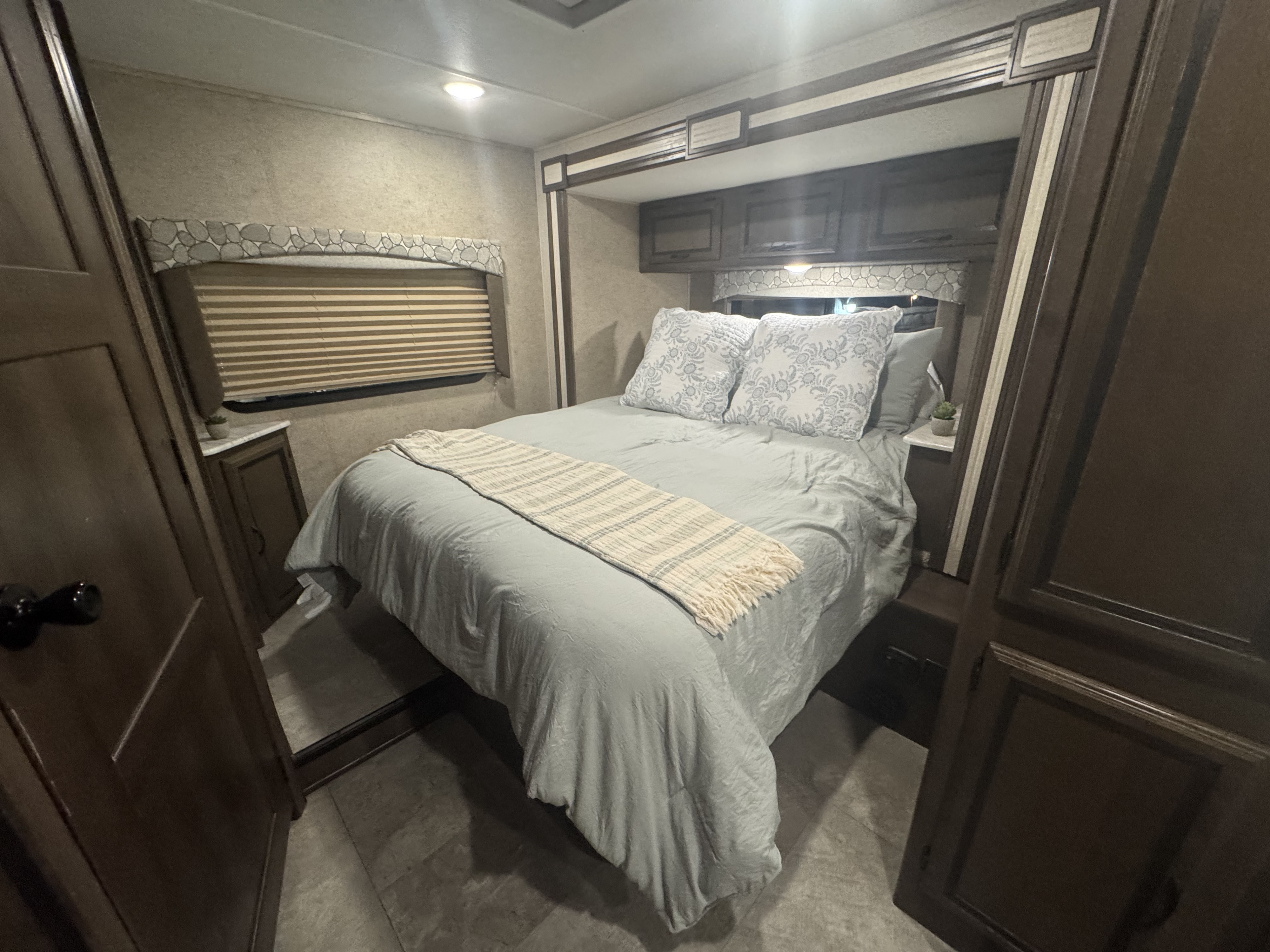 Comfortable RV rental bedroom space with light blue bedding, accent pillows, and overhead storage.. Coachman Freelander 26RS 2018