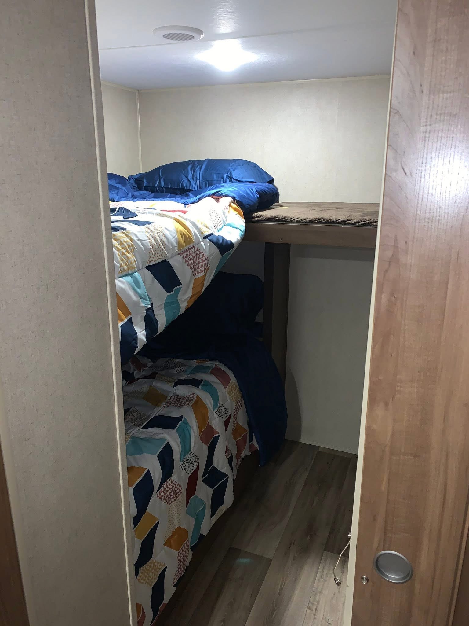 RV rental: Compact bunk bed sleeping area with two made beds, colorful bedding, and an upper empty bed frame.. Aspen Trail Aspen Trail Trailer 2018