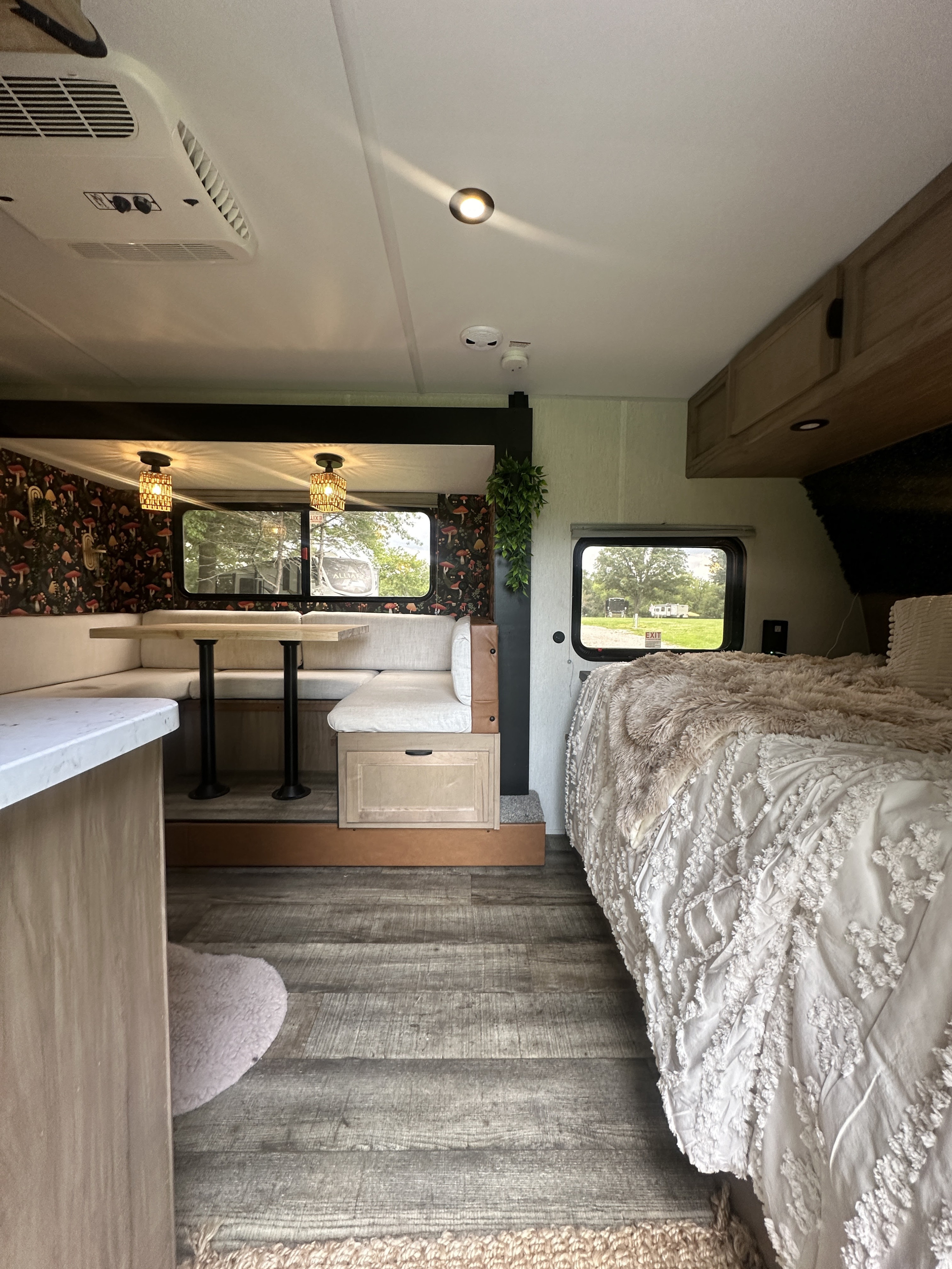 Cozy RV rental interior with a modern dining booth, mushroom accent wall, comfy bed, and wood-look flooring.. Forest River Cherokee Wolf Pup 2024