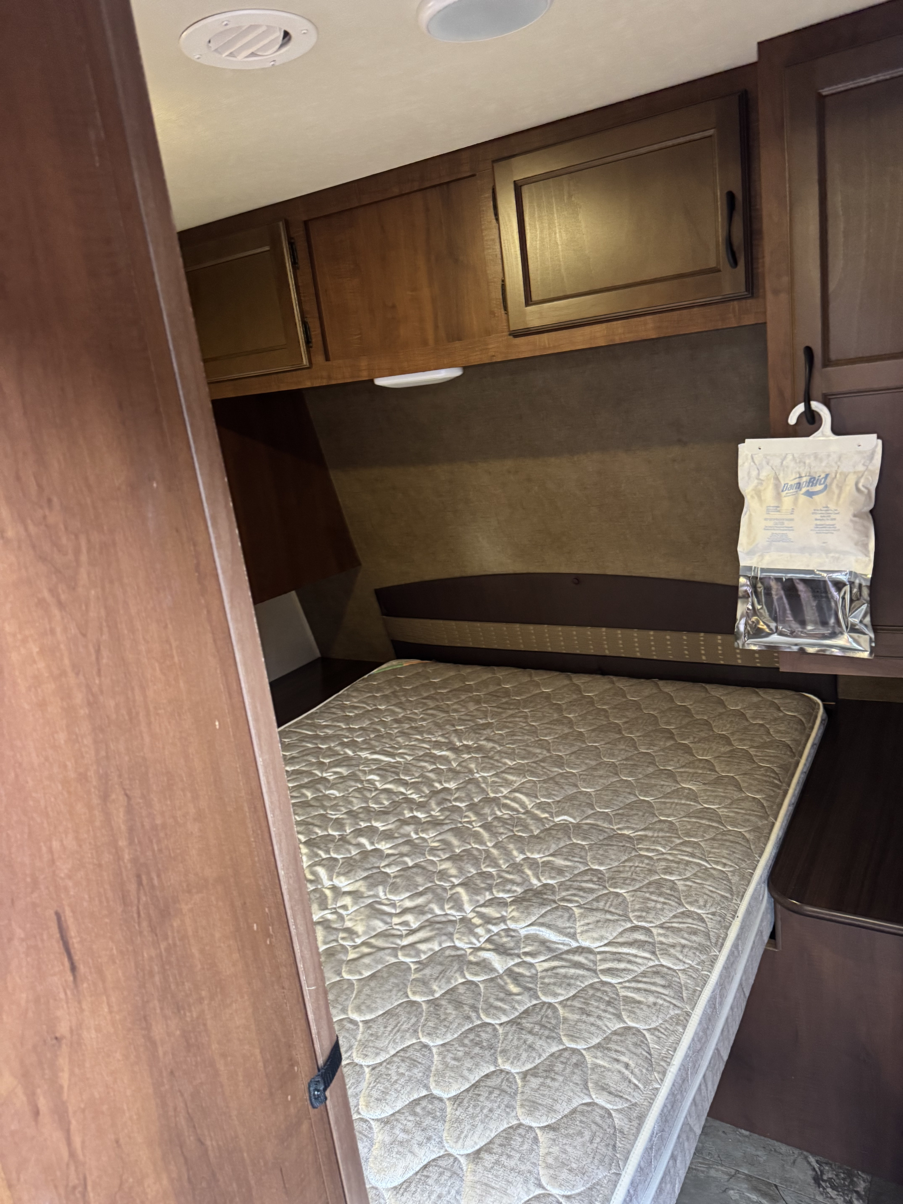 RV rental bedroom interior with a quilted bed, overhead storage, and a moisture absorber bag hanging from a cabinet.. Jayco Jay Flight 2015