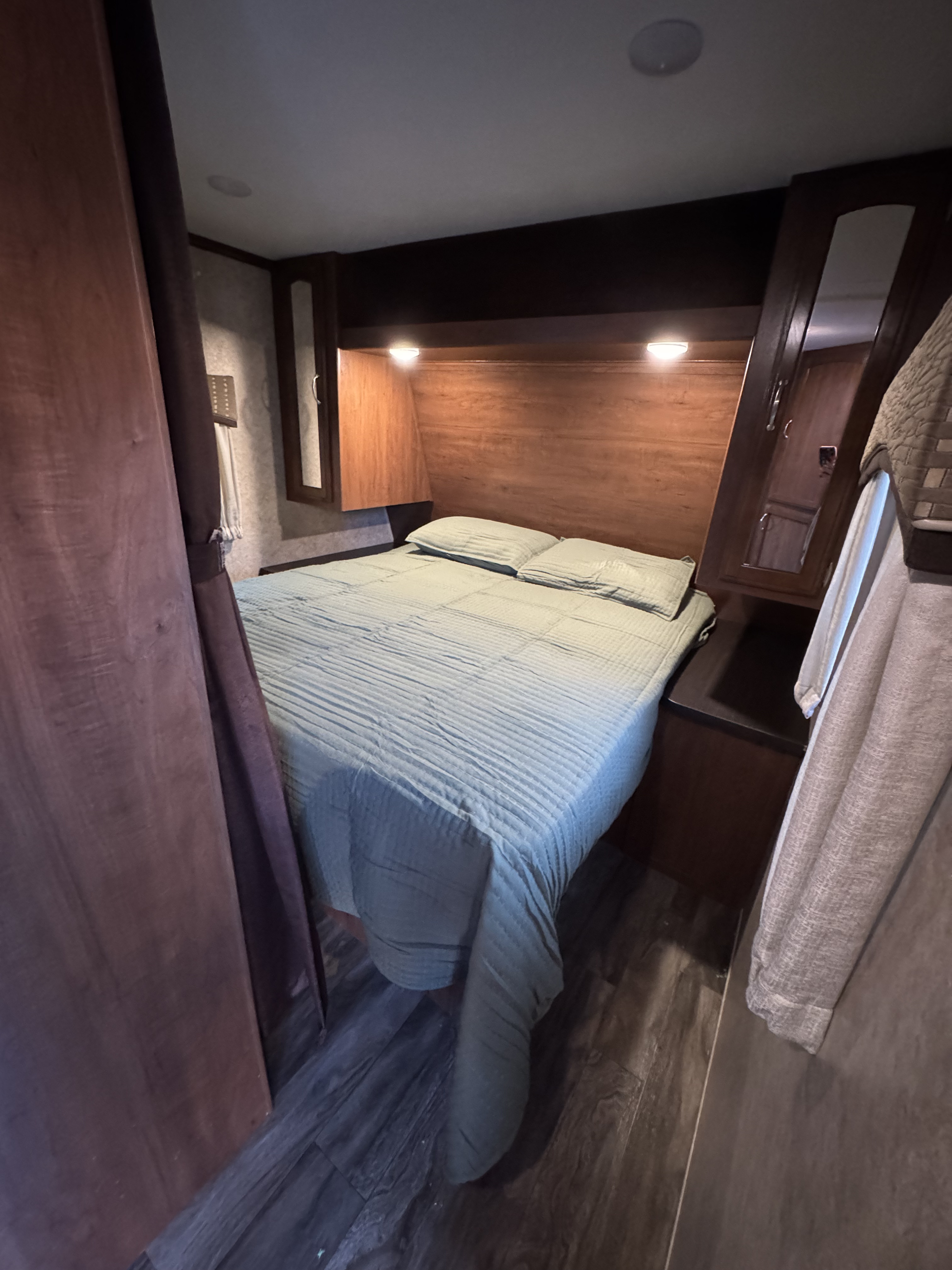 Inside a compact RV rental bedroom, featuring a neatly made bed, wooden headboard with accent lights, and mirrored cabinets.. Jayco Jay Feather 2017
