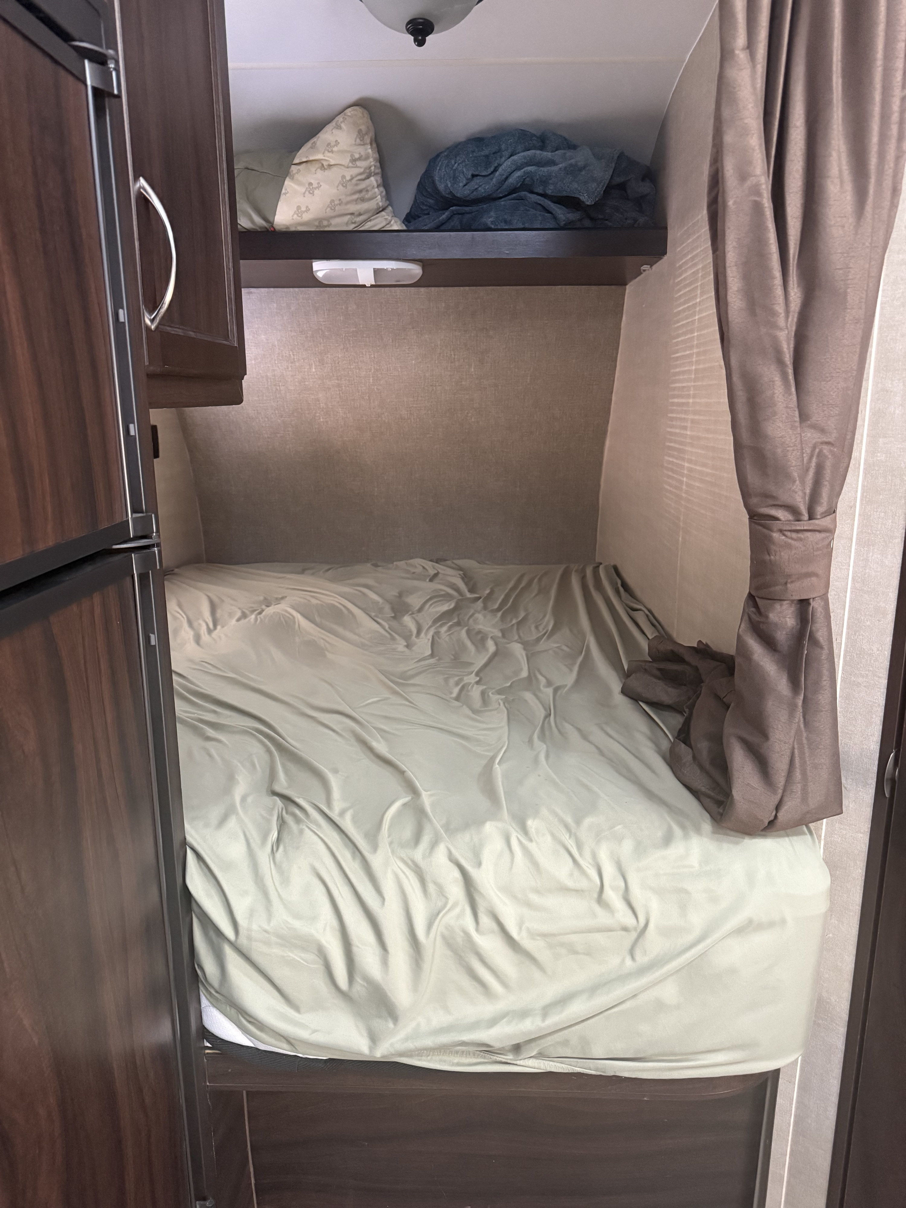 RV rental: Compact sleeping area with a light green bed, overhead shelf, and brown curtains.. Pacific Coachworks 24FSB 2017