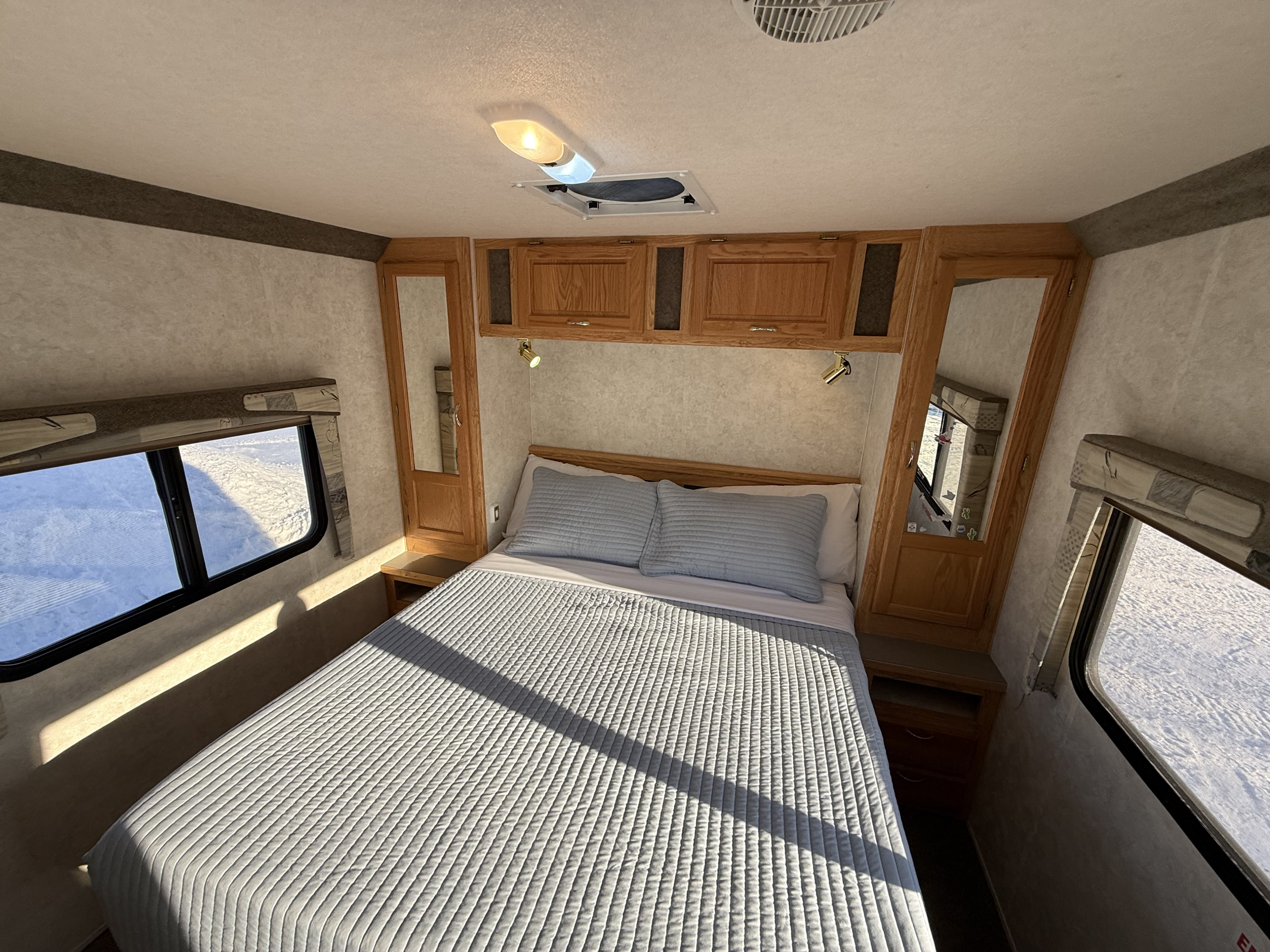 Cozy RV rental bedroom with queen bed, wooden cabinets, and snowy window views. Perfect for winter travel accommodation.. Bigfoot RV Bigfoot RV Motorhome 2004