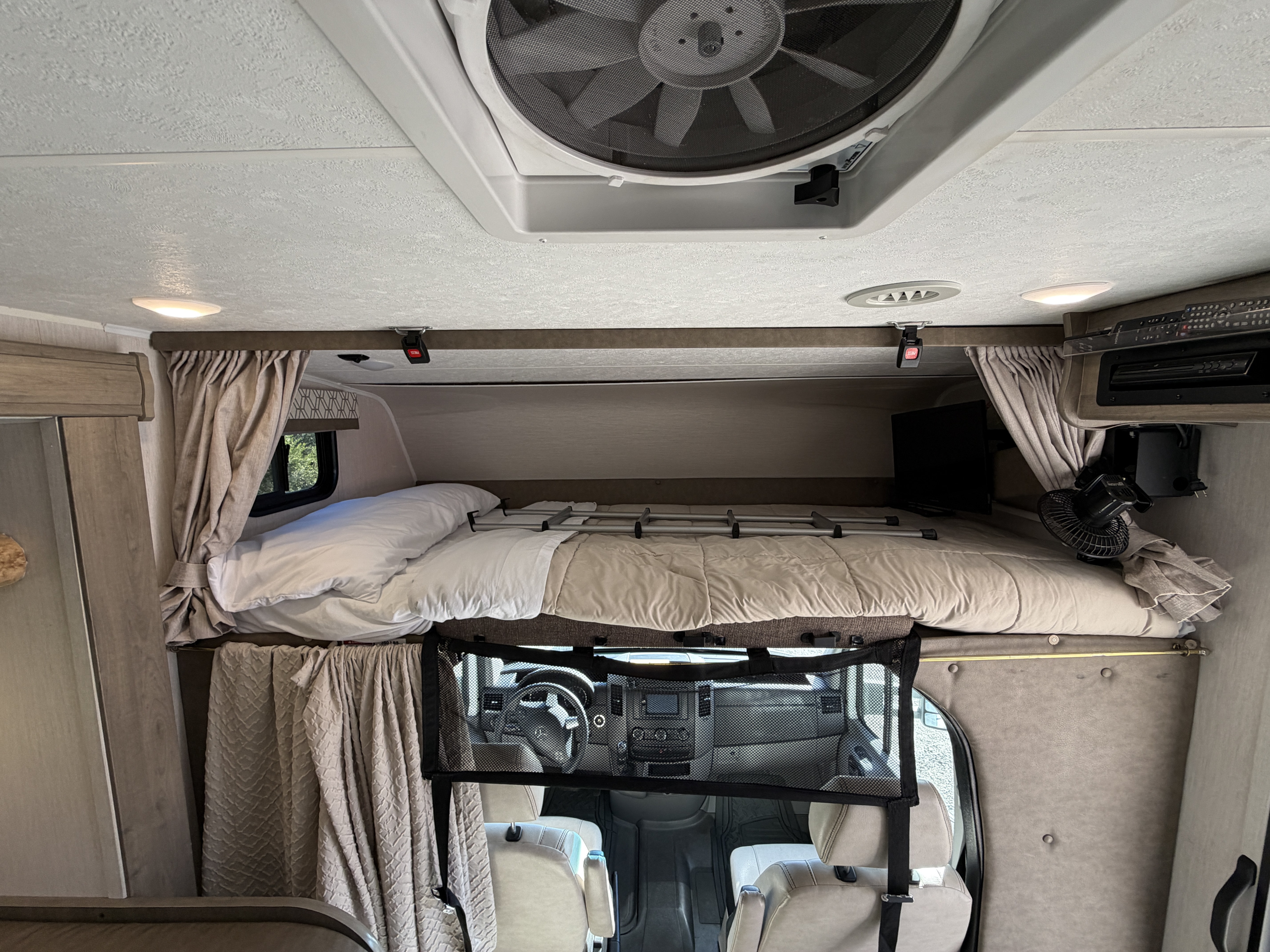 An RV rental's cozy interior features a cab-over bunk bed, ceiling fan, TV, and a view looking down into the cockpit.. Coachmen Other 2020
