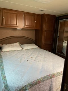 Step inside this cozy RV rental bedroom. Features a comfy bed, wood overhead cabinets, and a tall wardrobe with a mirrored door.. Forest River Coachmen Leprechaun 2015