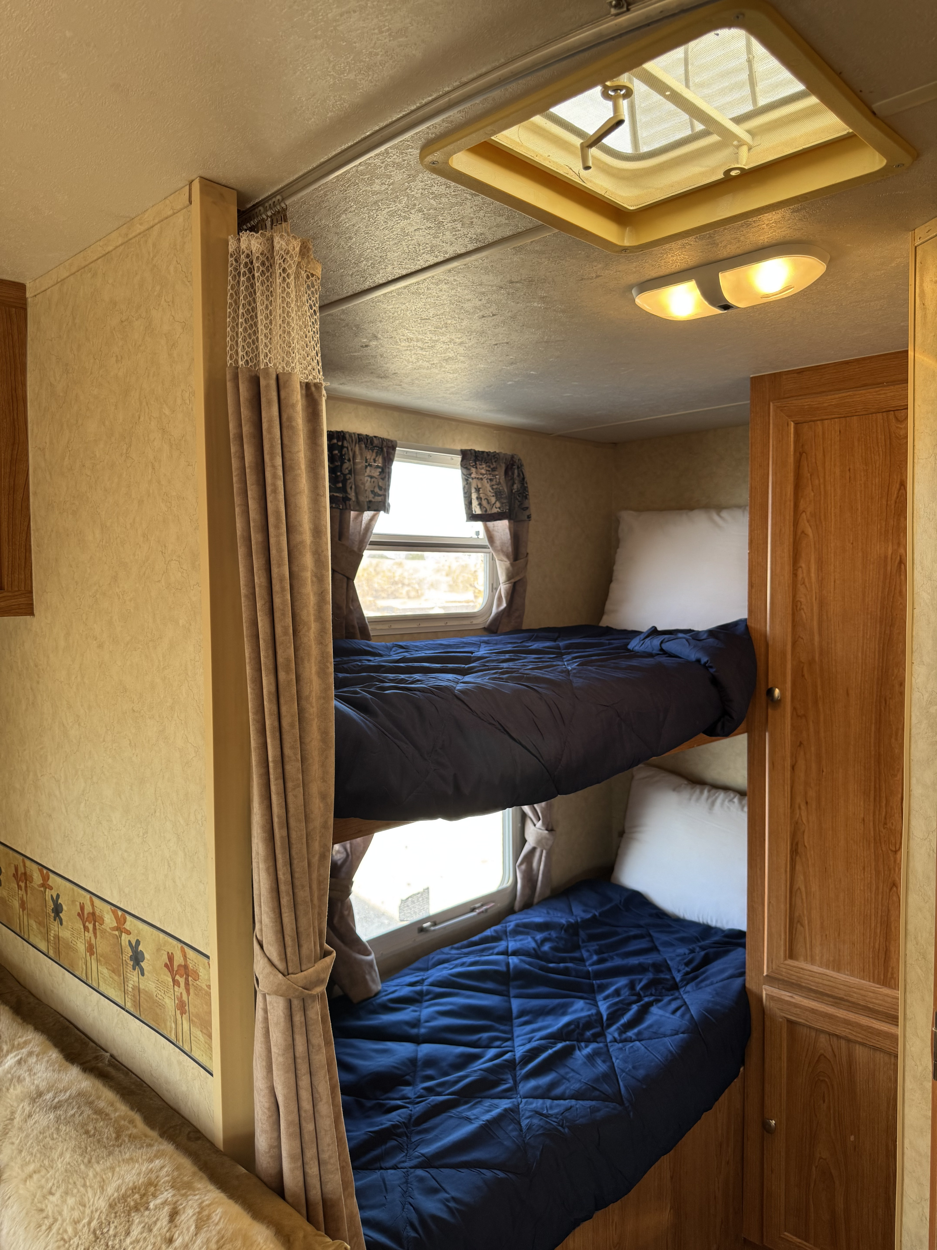 An inviting RV rental interior featuring two bunk beds with navy bedding, windows, and overhead lighting.. R-Vision Trail-Lite Trail-Sport 2006