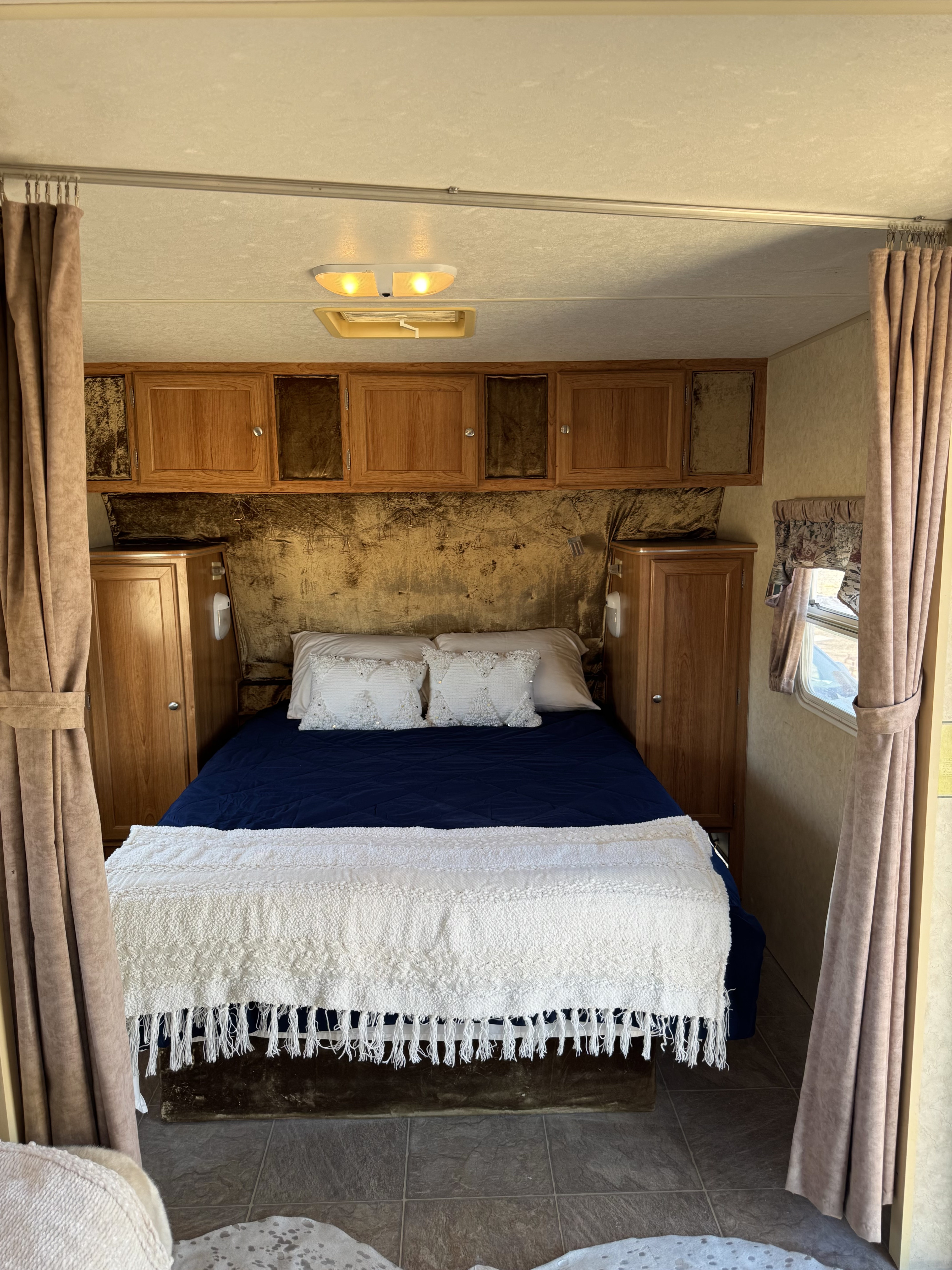 Cozy RV rental bedroom featuring a bed with navy and white bedding, wooden cabinets, and tan curtains.. R-Vision Trail-Lite Trail-Sport 2006
