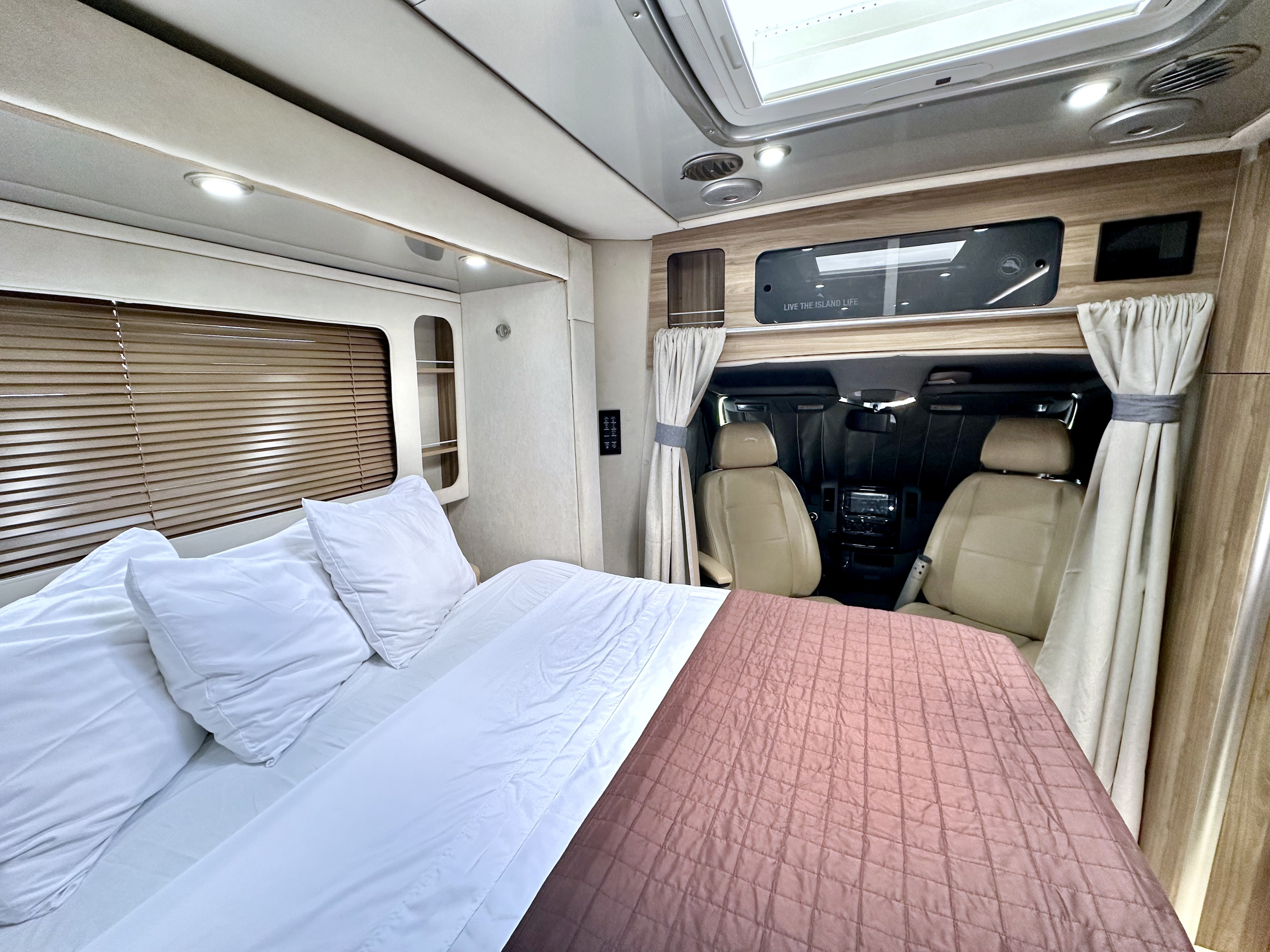 Cozy rv rental interior: A comfortable bed with white pillows and a pink quilt faces the driver's cabin, separated by curtains.. Airstream Atlas 2020