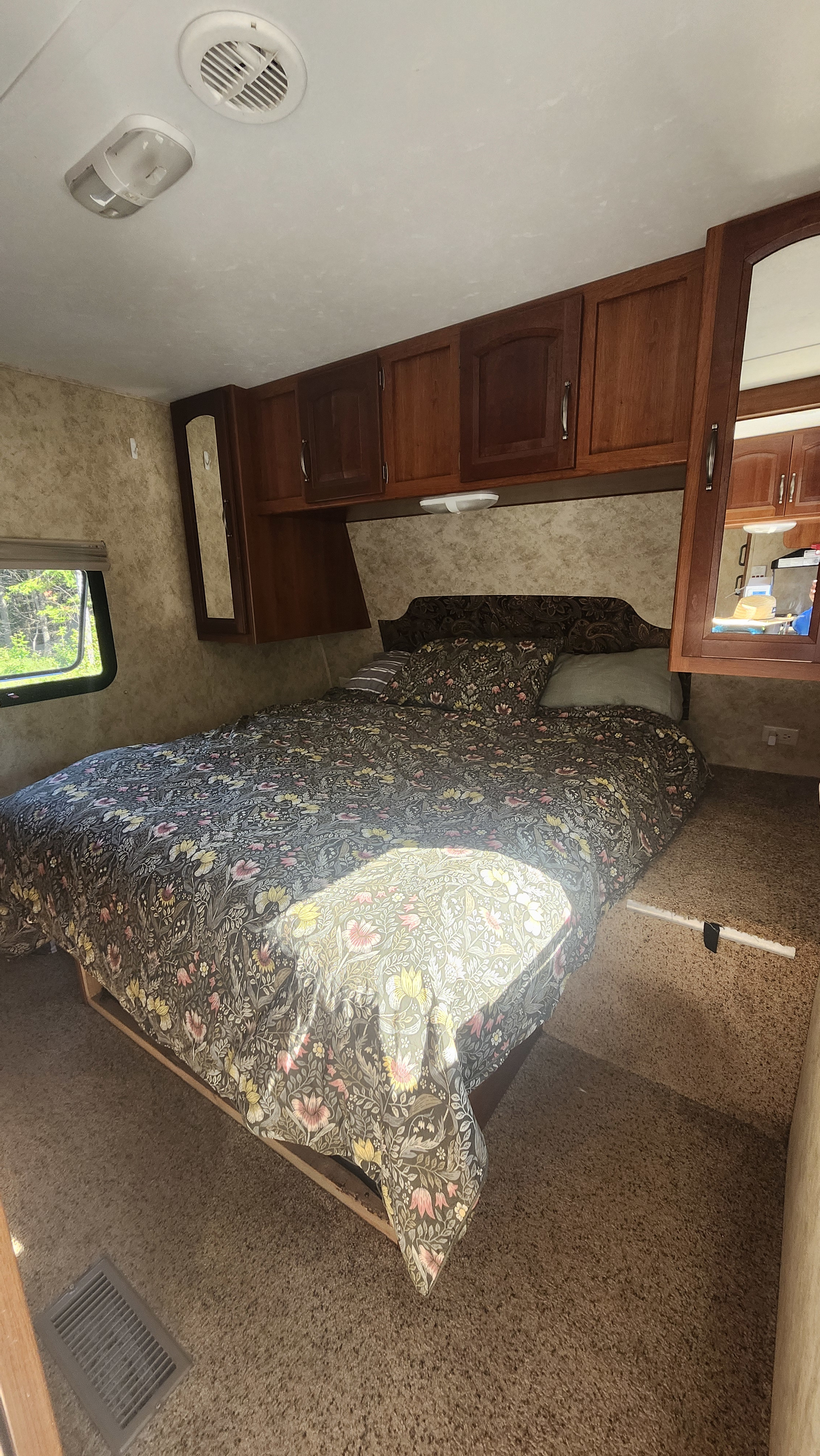 RV rental bedroom: cozy space with a floral bed, wooden overhead cabinets, and a window. Features a ceiling vent and light.. Keystone RV Cougar 2011