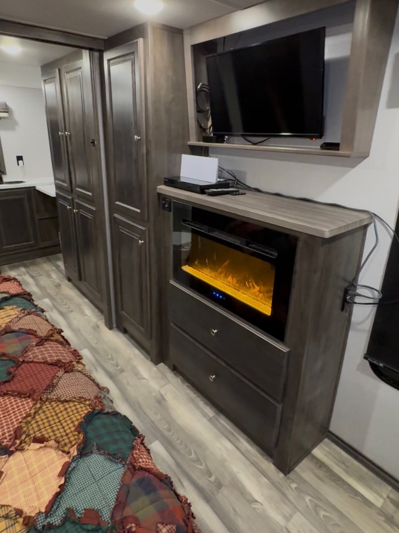Cozy rv rental interior with a TV, electric fireplace, dark wood cabinetry, and a colorful patchwork quilt on the floor.. Forest River Cardinal 2021