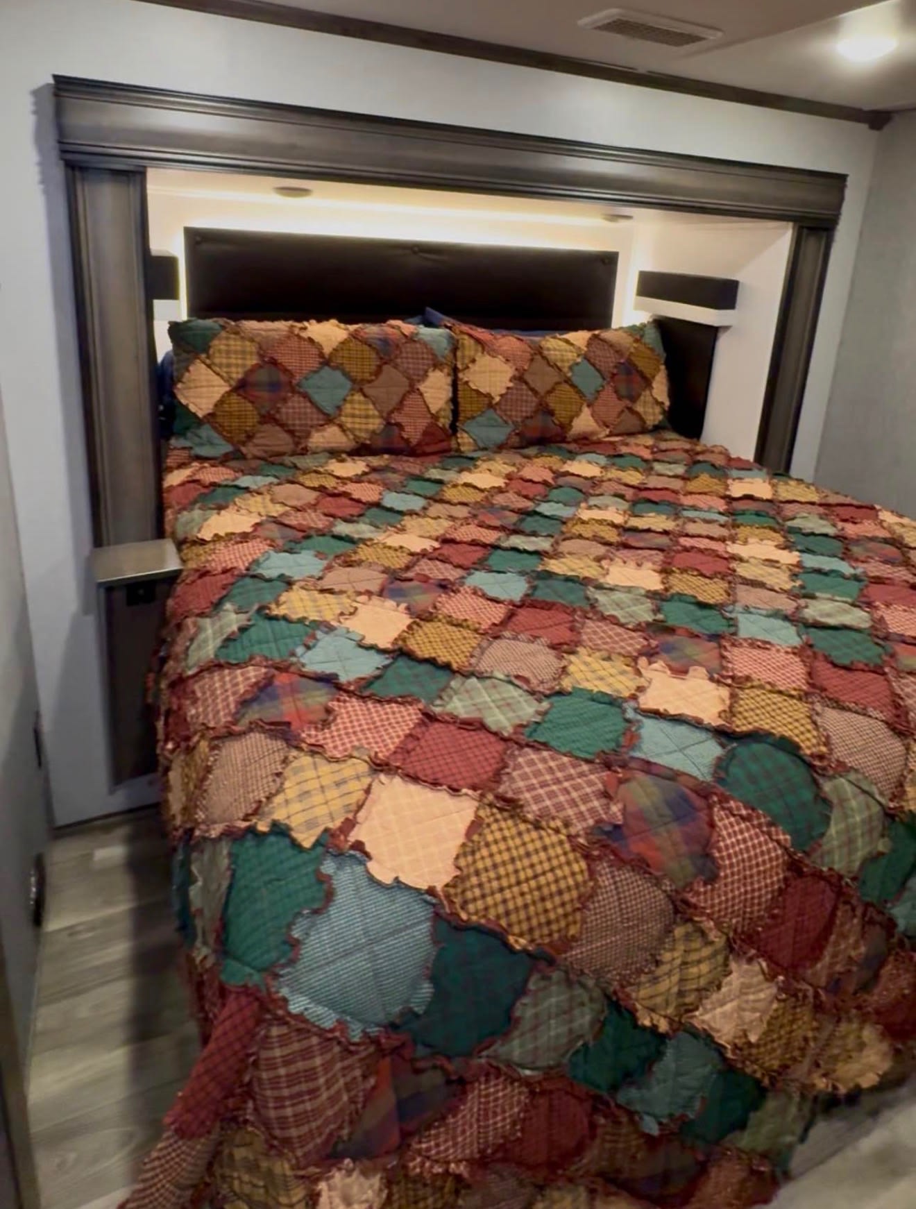 Cozy RV rental bedroom with a rustic patchwork quilt and soft lighting, perfect for a relaxing stay.. Forest River Cardinal 2021