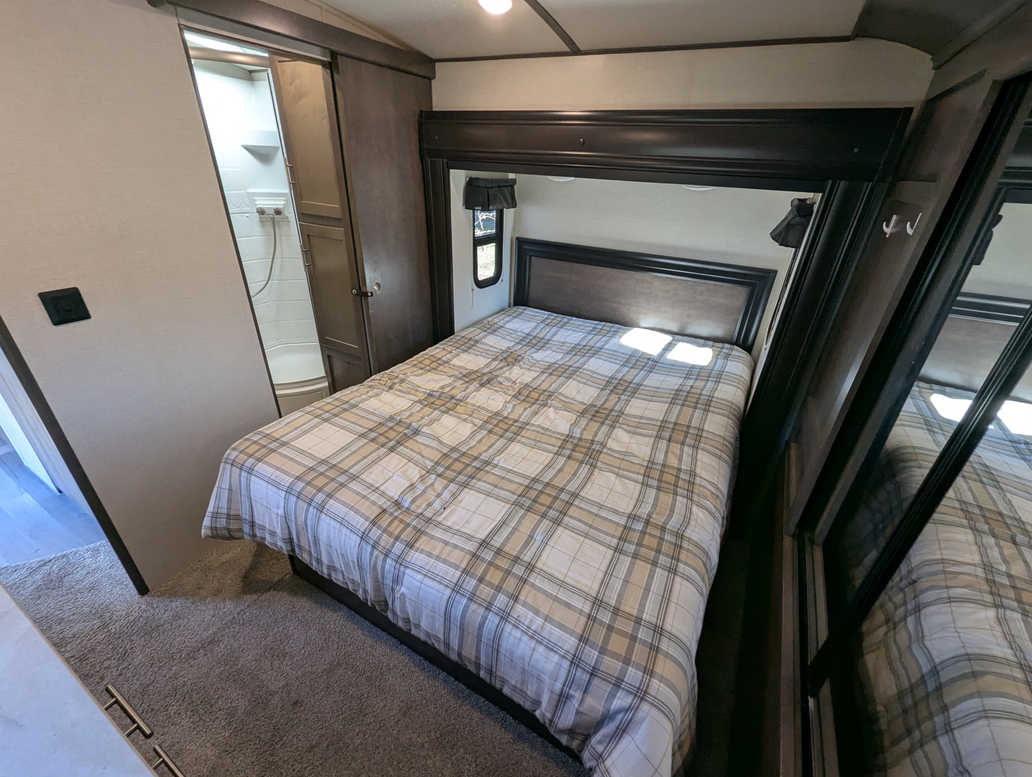 RV rental bedroom with a cozy plaid-covered bed, dark wood headboard, window, and adjacent shower/closet.. Crossroads RV Sunset Trail Super Lite 2018