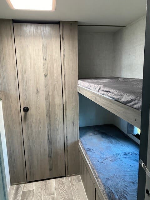 RV rental bedroom features two cozy bunk beds (top grey, bottom blue) and a light wood-grain closet.. Gulf Stream Ameri-Lite 2023