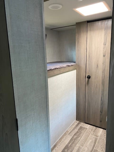 Peek inside an rv rental: compact sleeping area with bunk beds, adjacent wood-look closet, and light flooring.. Gulf Stream Ameri-Lite 2023
