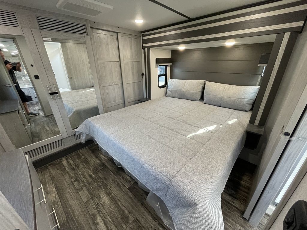 Modern rv rental bedroom featuring a large bed with grey bedding, built-in storage, and reflective wardrobe doors. Ready for travel.. Keystone RV Fuzion Toy Hauler 2021