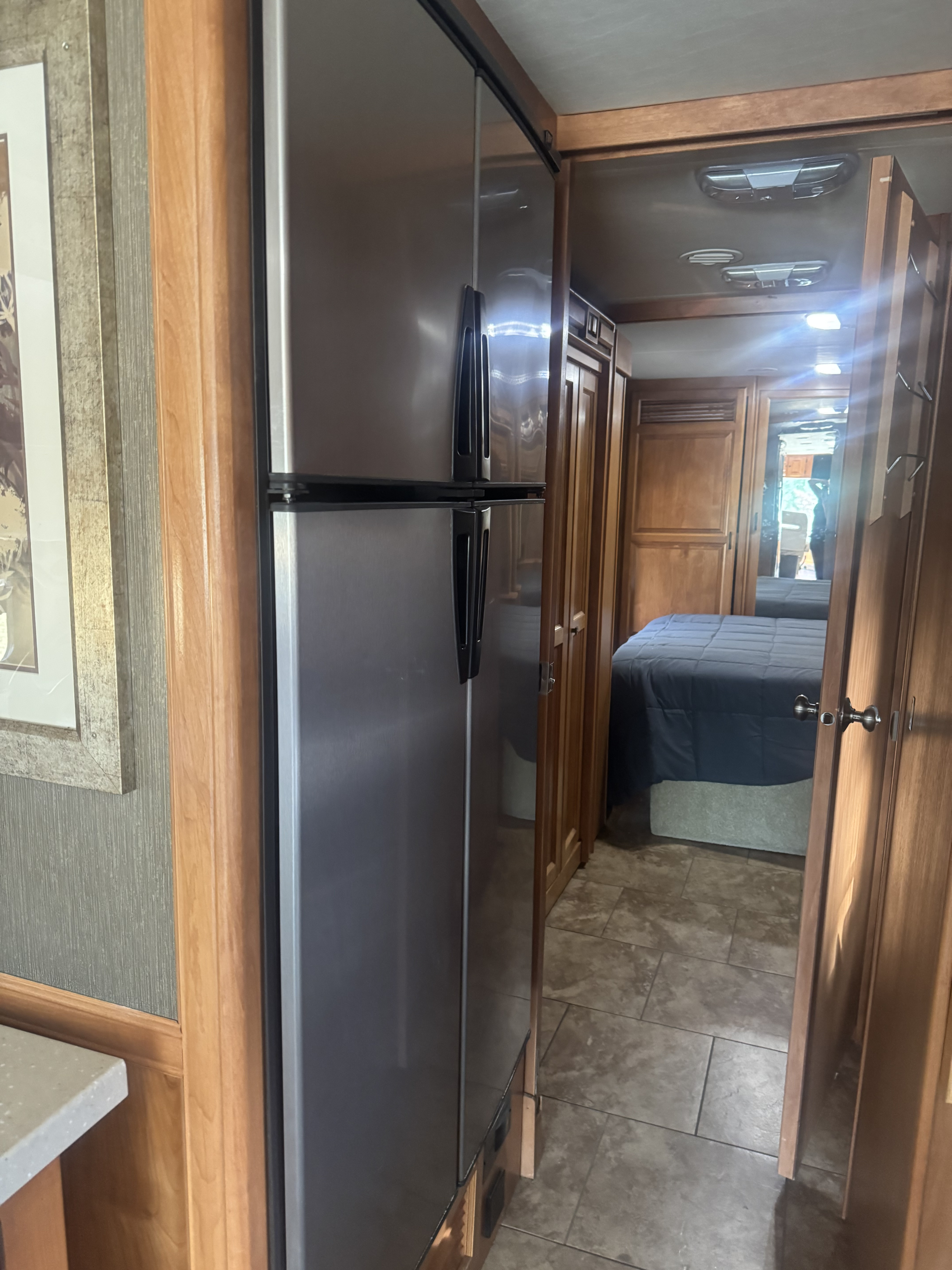 RV rental interior view: stainless steel refrigerator, wood-paneled hallway to a cozy bedroom with a dark blue comforter.. Tiffin Allegro 2013