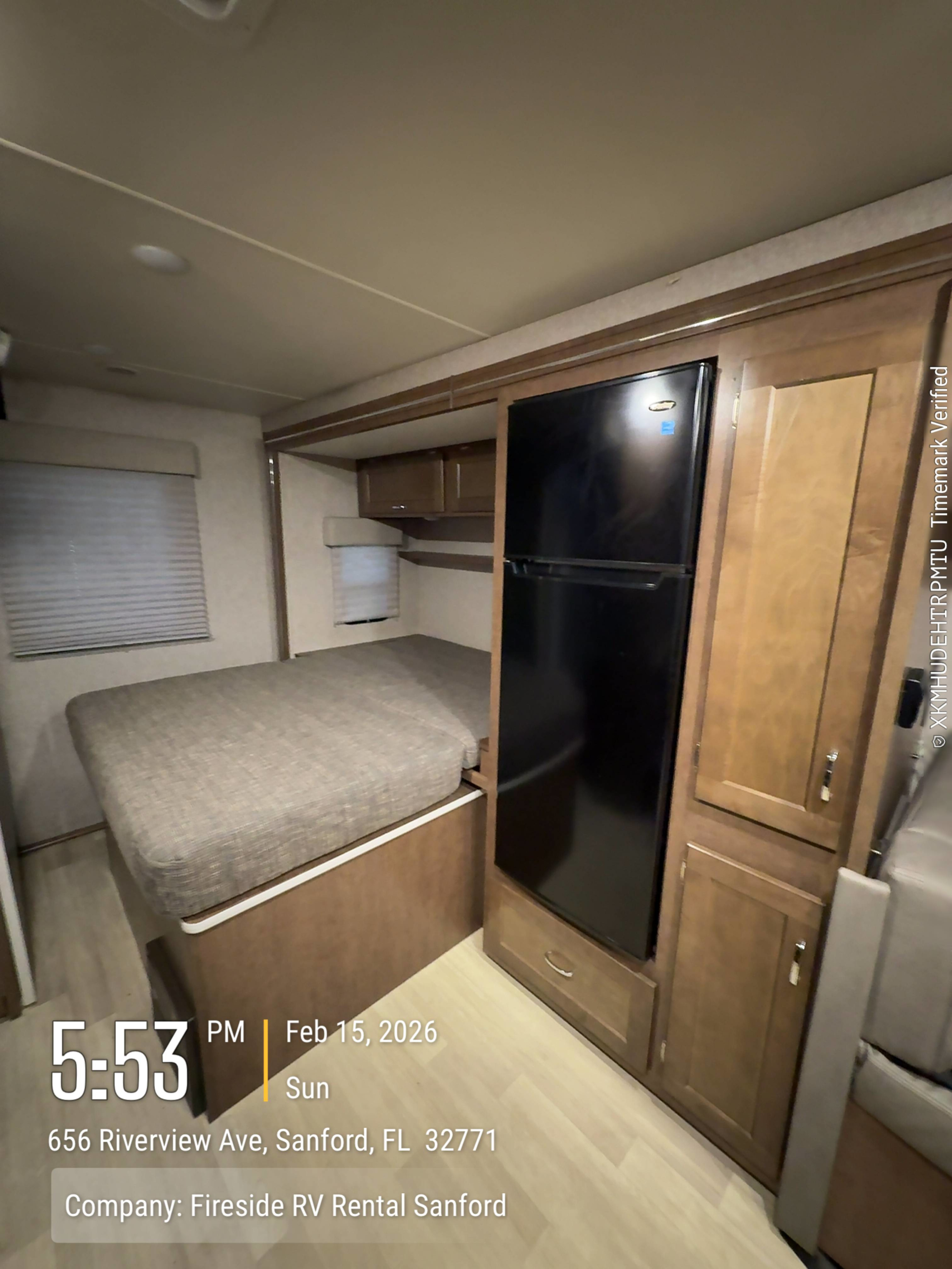 Interior of an RV rental from Fireside RV Rental Sanford, showing a bed, black refrigerator, and wood cabinetry.. Winnebago Porto 2020