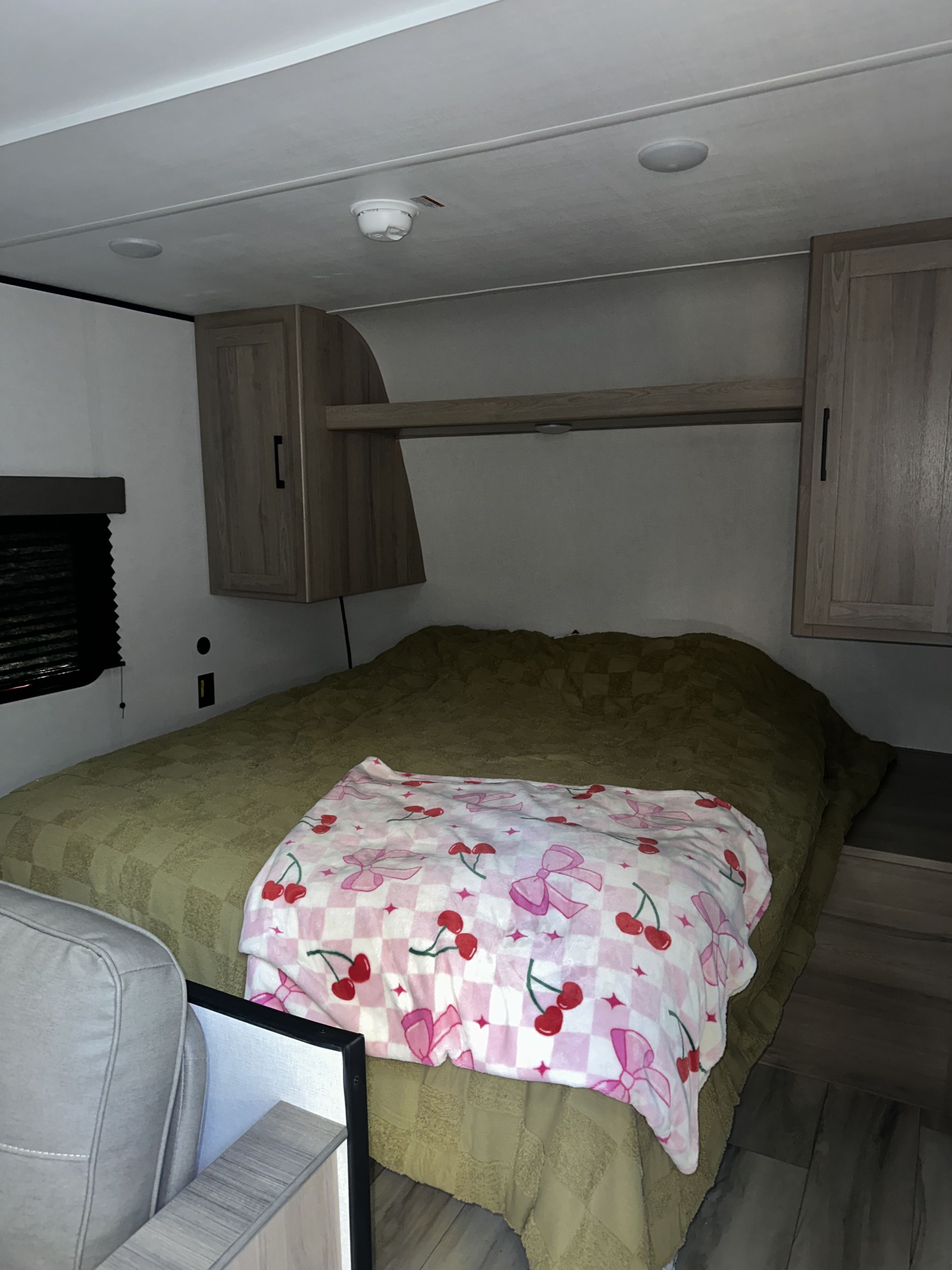 Cozy RV rental bedroom featuring a bed with a green comforter, a pink cherry blanket, and overhead storage cabinets.. Keystone RV Coleman 2025