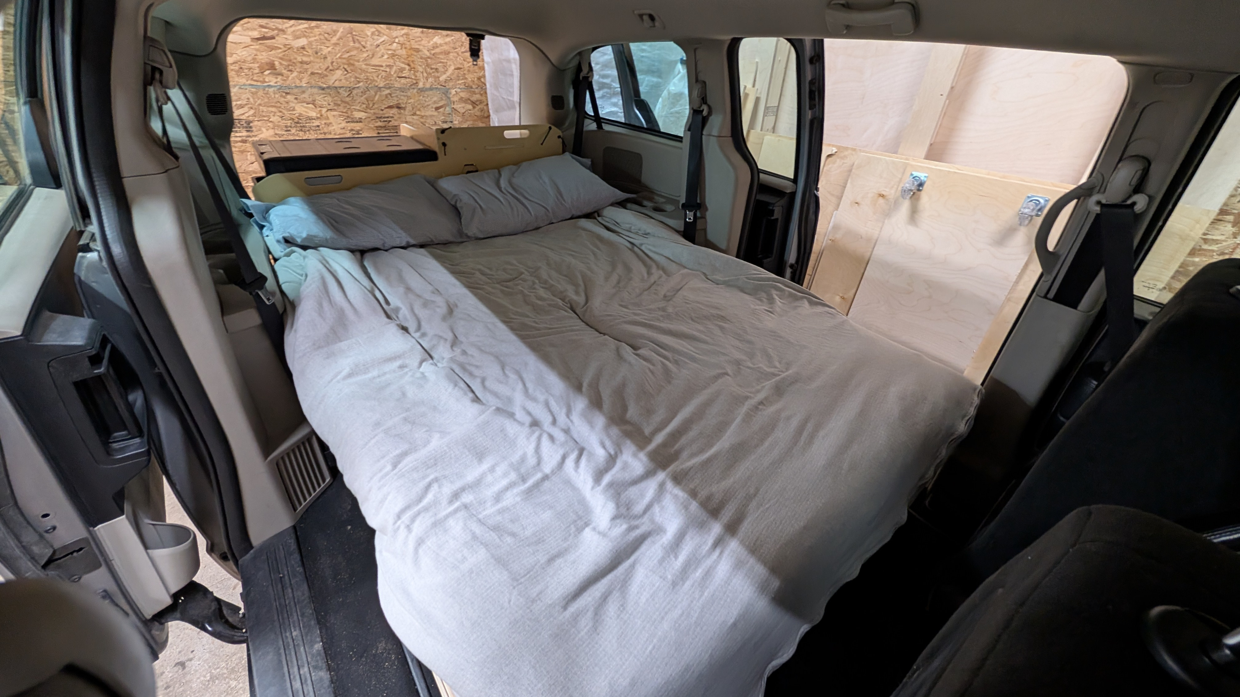 Cozy bed setup in a minivan RV rental conversion, featuring custom plywood interior panels for comfortable travel.. Dodge Grand Caravan 2016