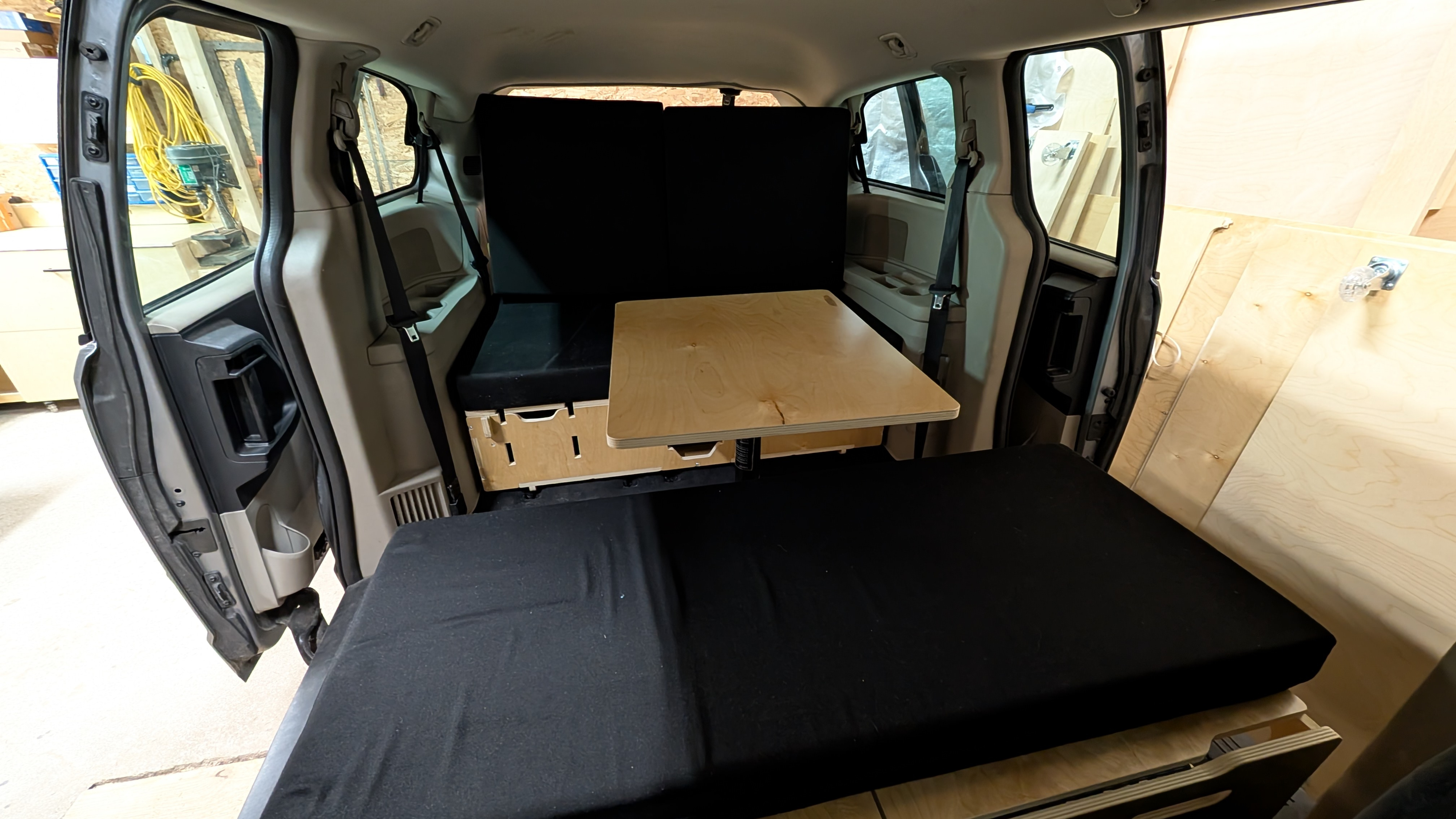 DIY camper van conversion in a minivan, featuring a bed, table, and storage. Perfect for rv rental travel.. Dodge Grand Caravan 2016