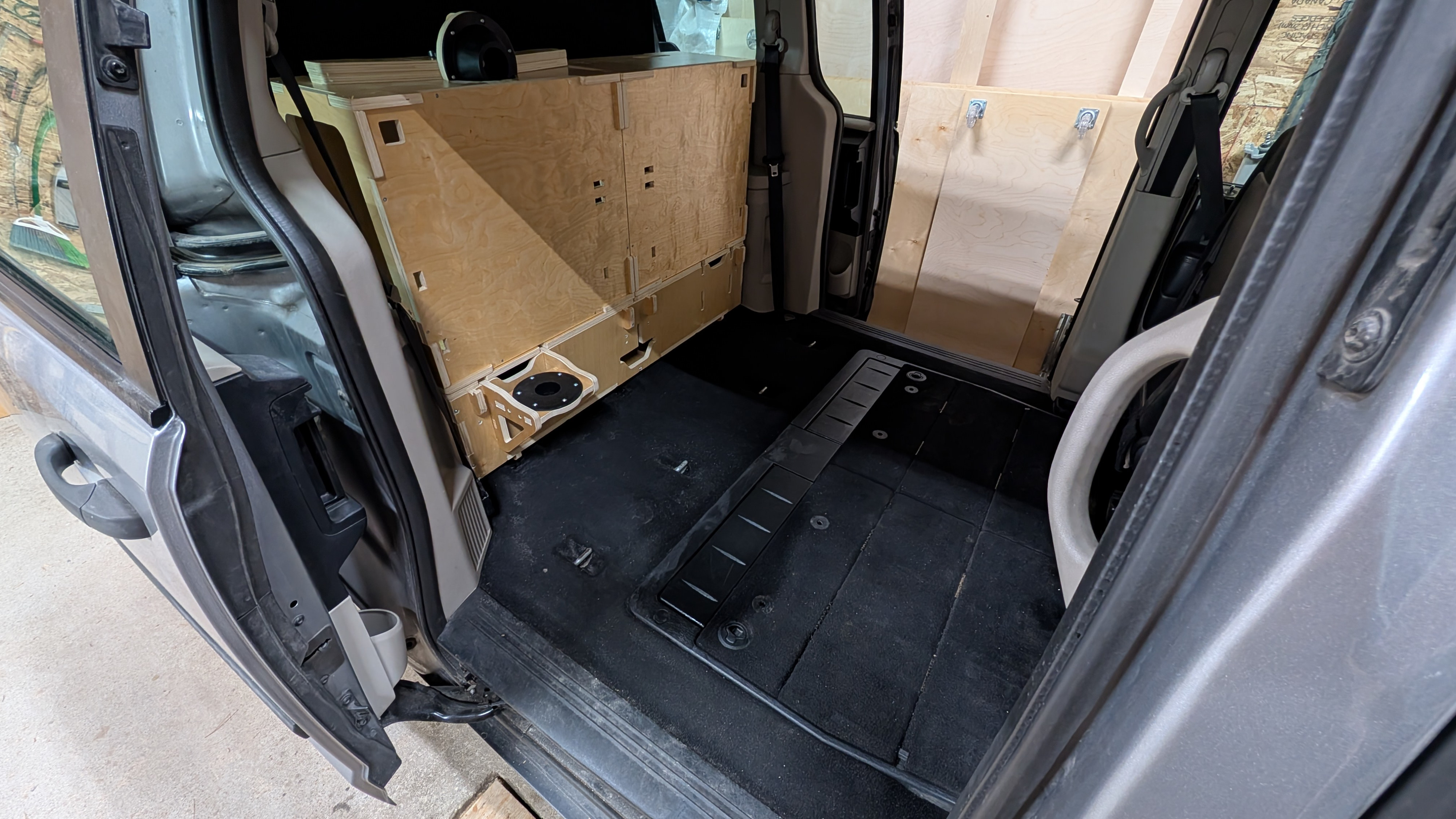 RV rental interior: custom wood cabinetry in a converted minivan, with floor mats and plywood side panels visible.. Dodge Grand Caravan 2016