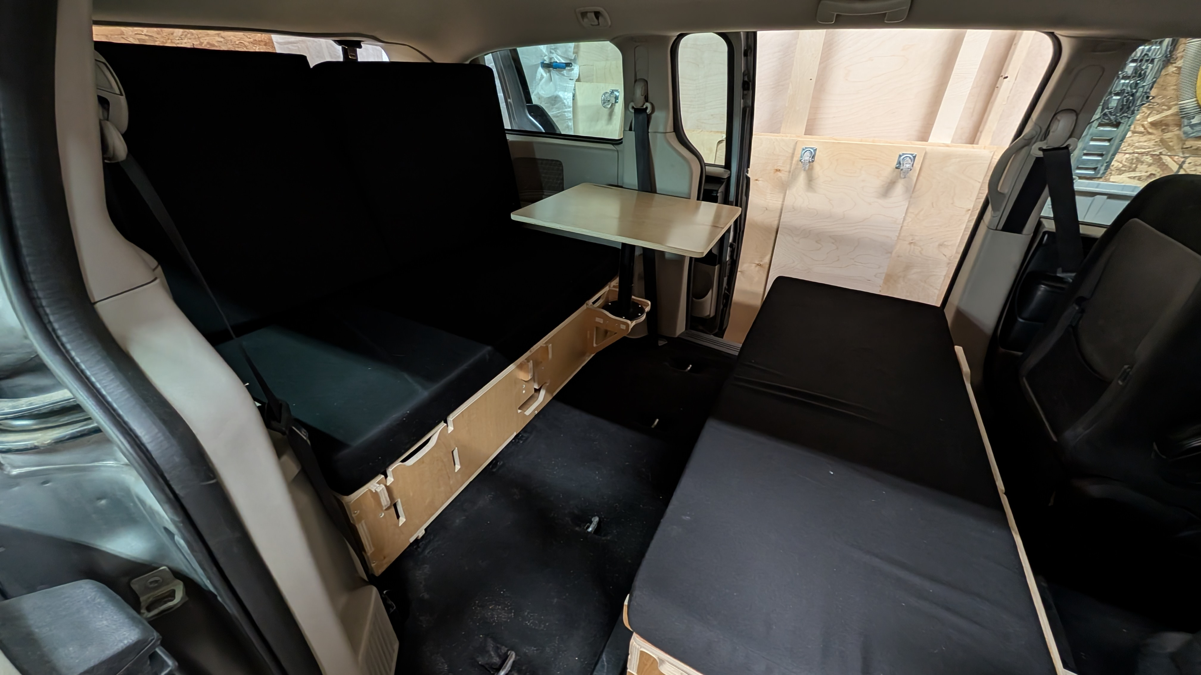 Rv rental van conversion interior with a comfortable bed, functional table, and custom storage for camping trips.. Dodge Grand Caravan 2016
