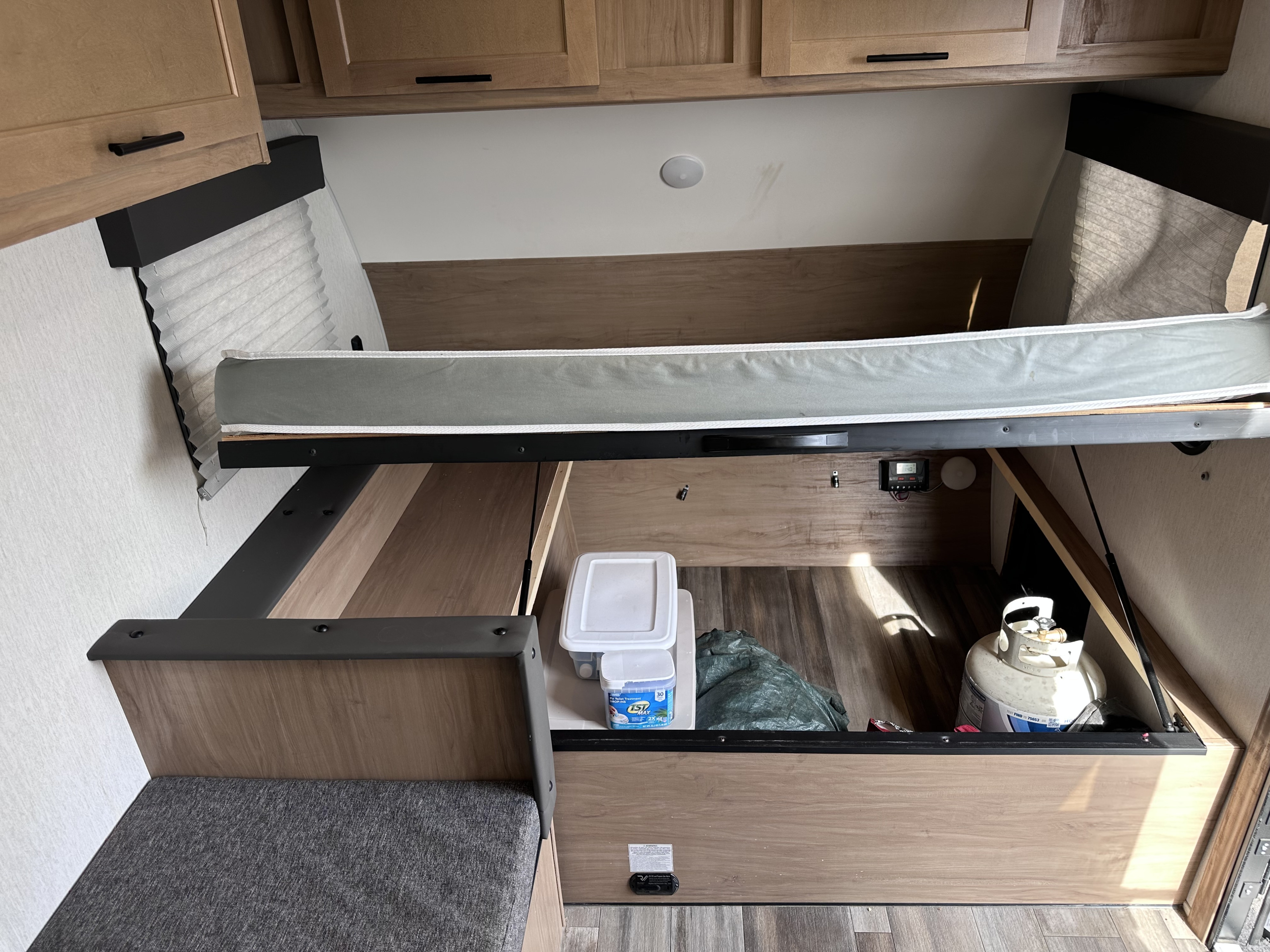 RV rental interior: lifted bed reveals under-bed storage with propane tank, containers, and control panel. Overhead cabinets.. Forest River Cherokee Wolf Pup 2023