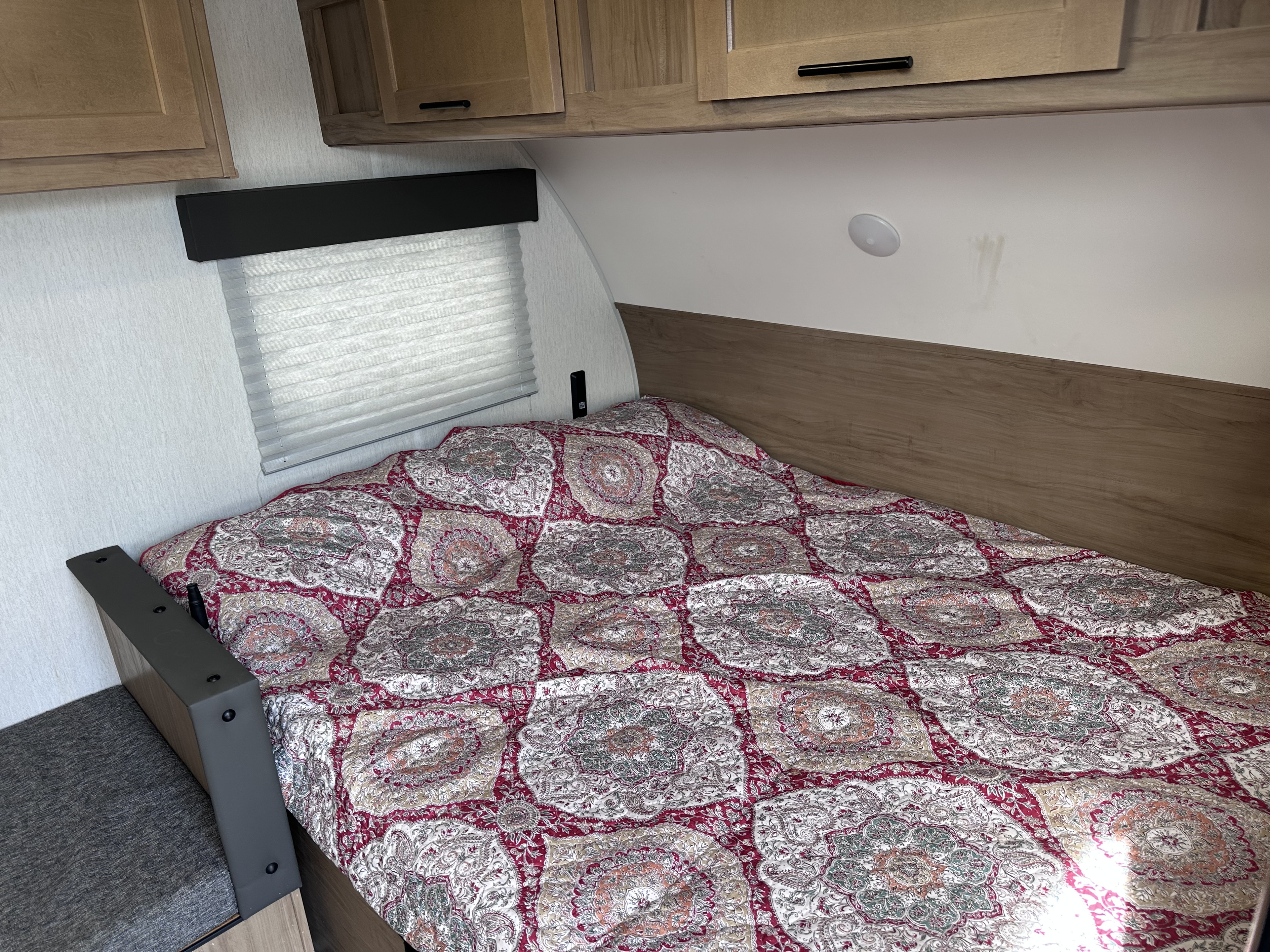 Cozy RV rental bedroom with a detailed patterned comforter, overhead cabinets, window blinds, and a small seating area.. Forest River Cherokee Wolf Pup 2023