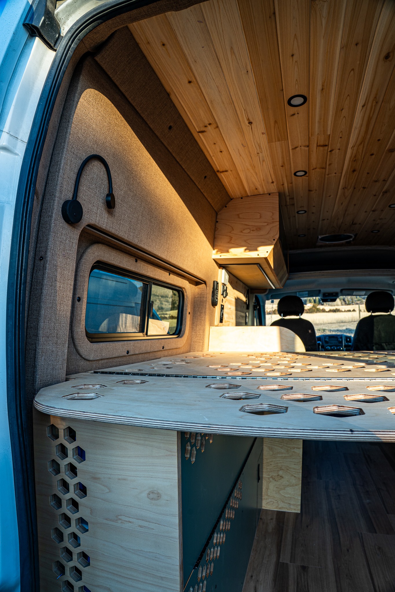 Explore this custom **rv rental** interior. Features a warm wooden ceiling, unique perforated bed platform, and cozy fabric walls.. Ram Promaster 2015