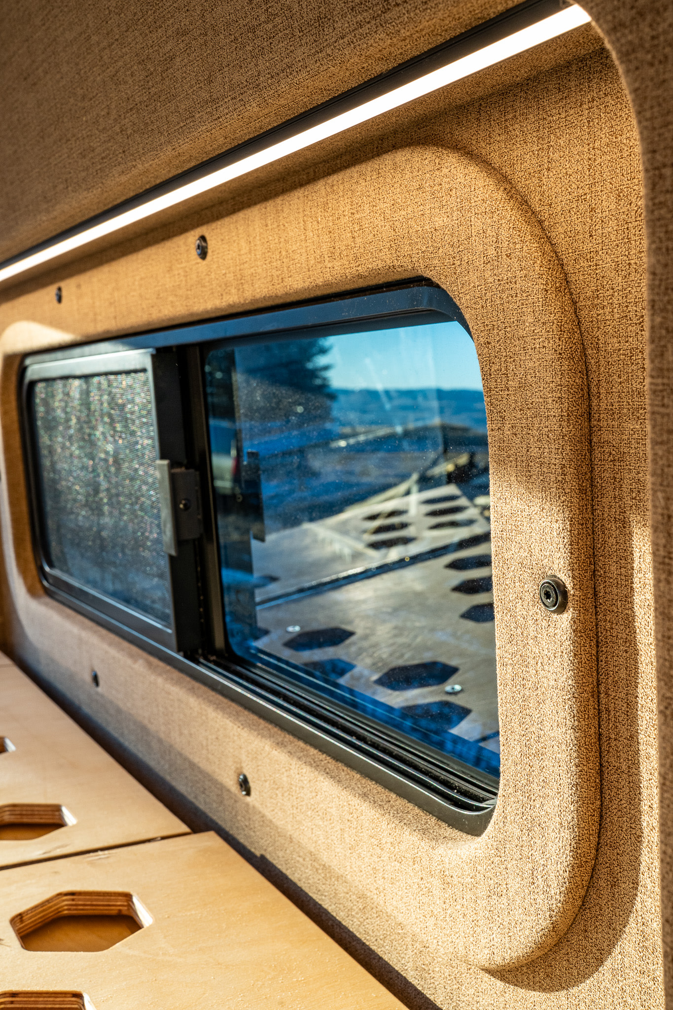 Inside an RV rental: a window offering nature views, sleek LED lighting, and a modular wooden bed platform. Ready for adventure.. Ram Promaster 2015