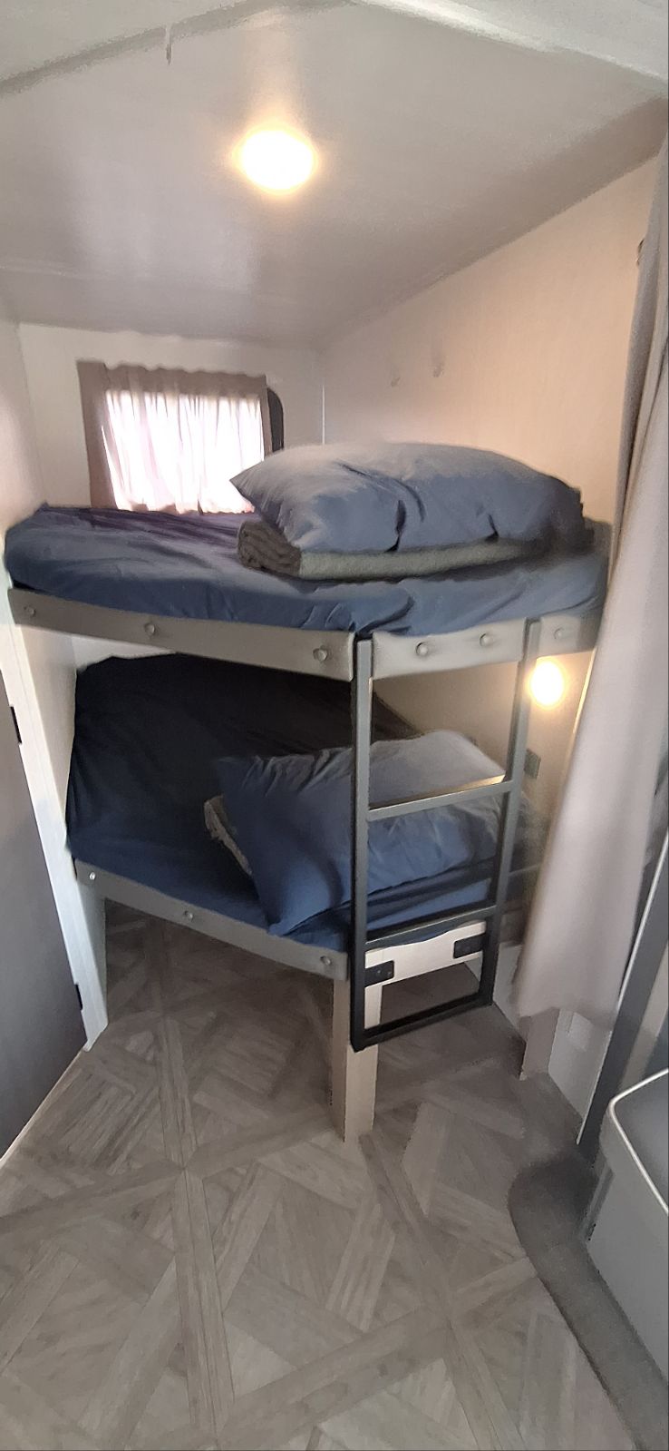Inside an RV rental, these compact bunk beds with blue bedding provide a functional sleeping area. Note the window and ceiling light.. Salem 26DBUD 2023