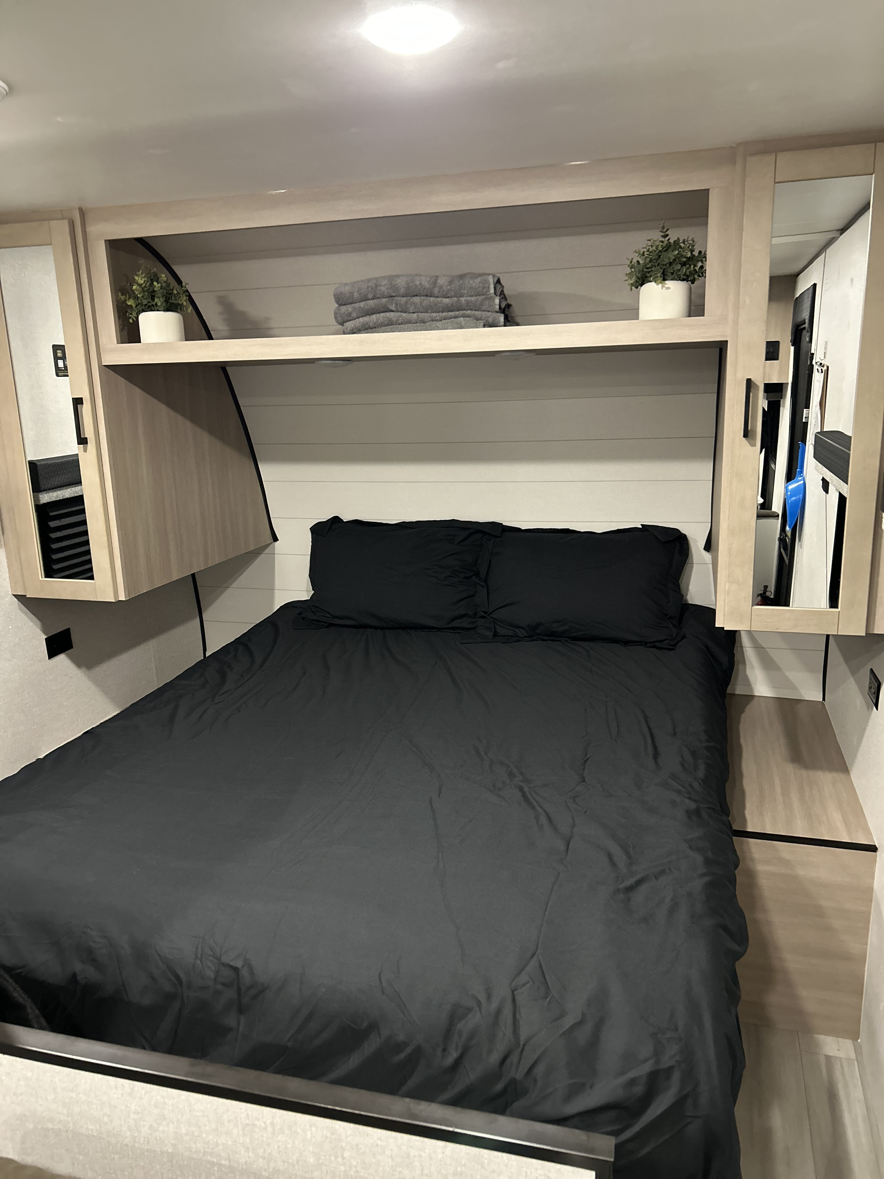 Modern rv rental sleeping area featuring a comfortable black bed, overhead shelving, and practical mirrored storage units.. Jayco Open Range 2026