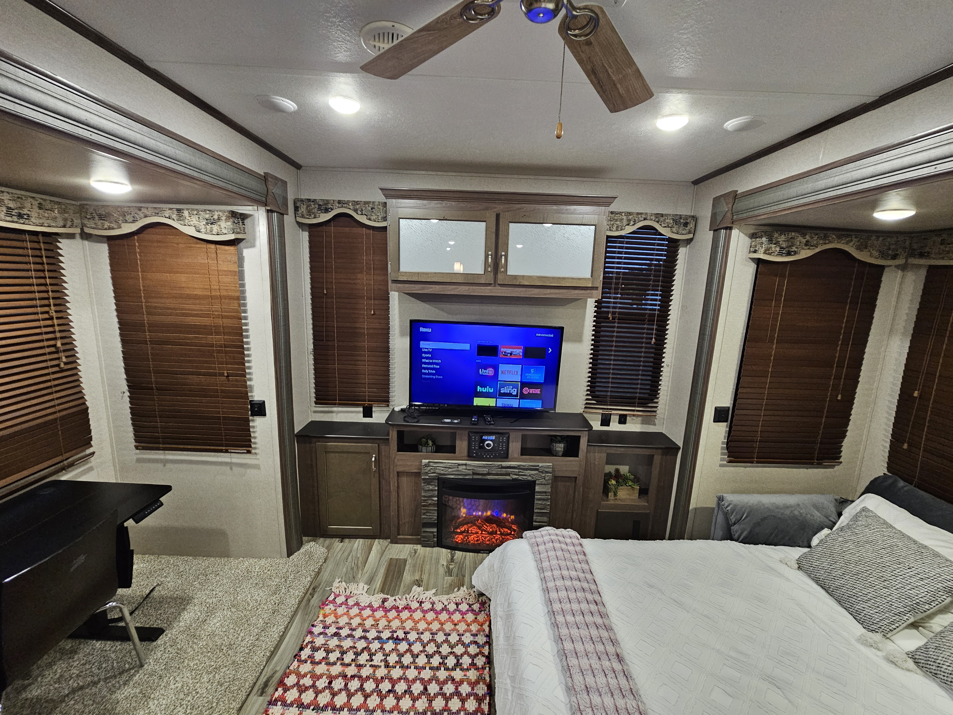 Cozy rv rental interior: bedroom area with TV, electric fireplace, ceiling fan, and a workspace with a desk.. Keystone Retreat 2019