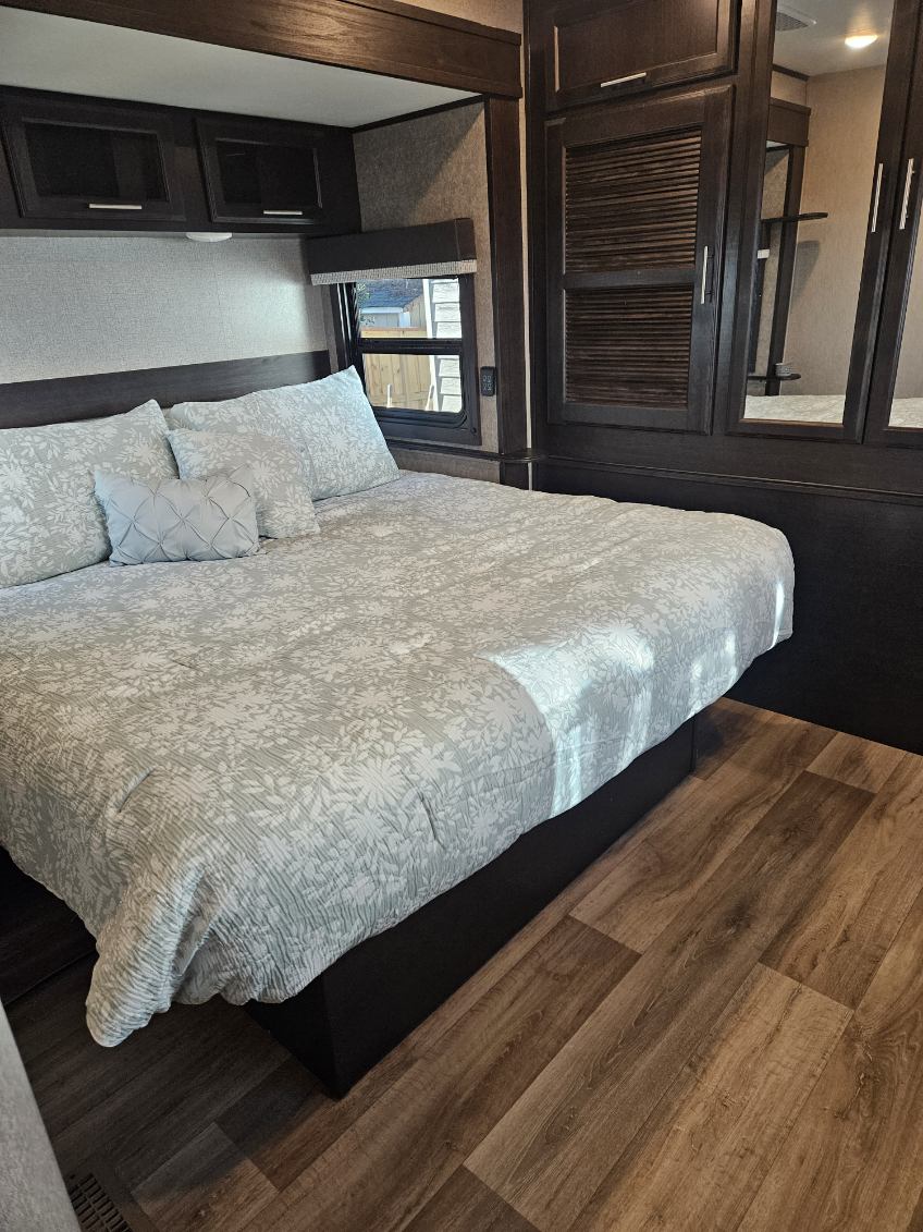 Spacious RV rental bedroom with a comfy queen bed, patterned bedding, dark wood cabinets, and laminate flooring.. Jayco Eagle 2021