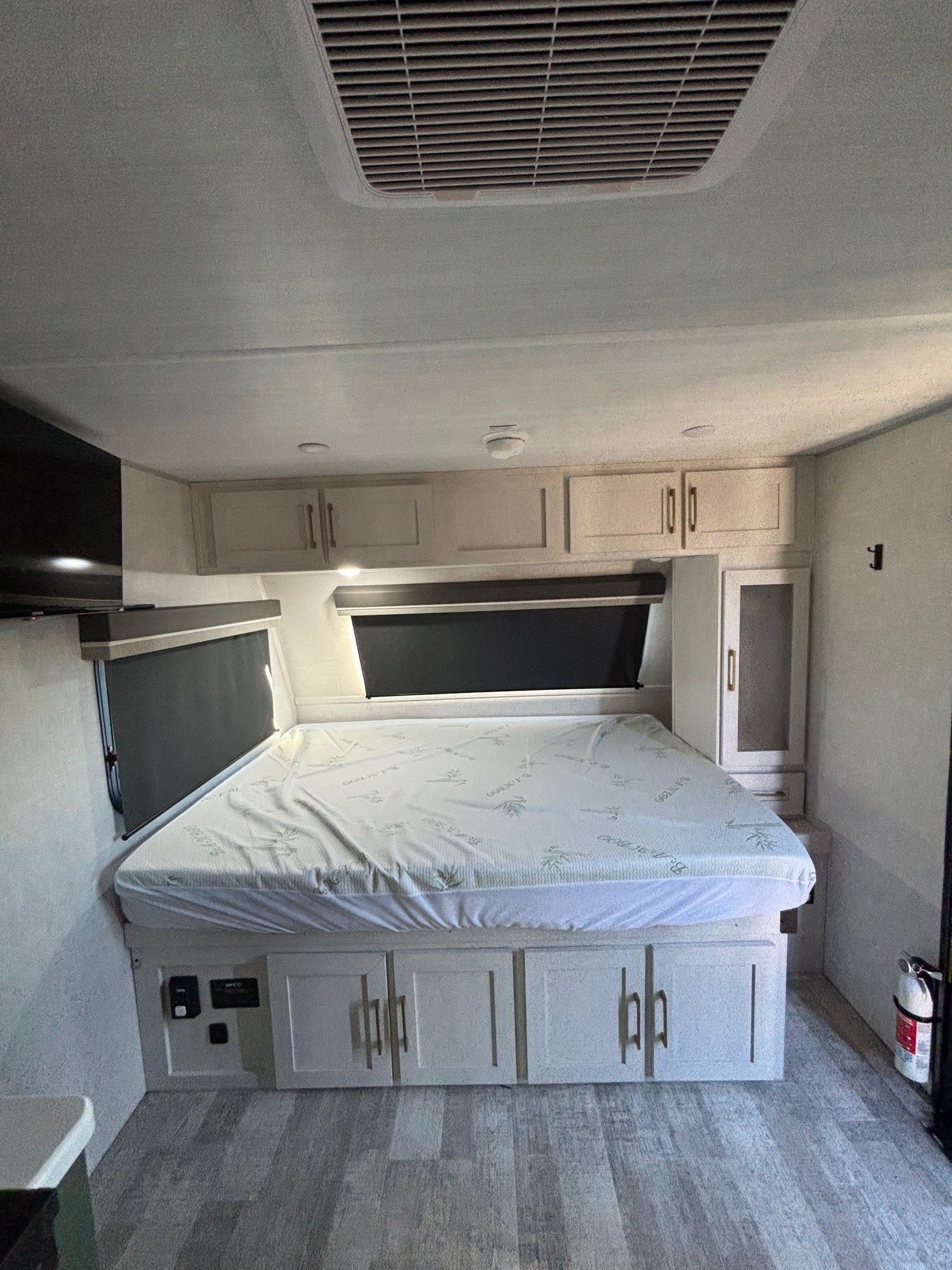 This RV rental bedroom features a comfortable bed, ample storage cabinets above and below, dark window blinds, and a TV.. No Boundaries 18 2025